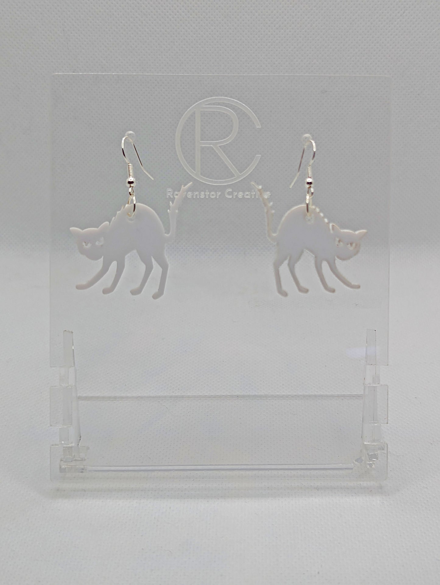 An image of a pair of earrings with black fixings on a white background, they are angry or scared looking cats in white with thier heckles and tails up and fir on end. Great for Halloween