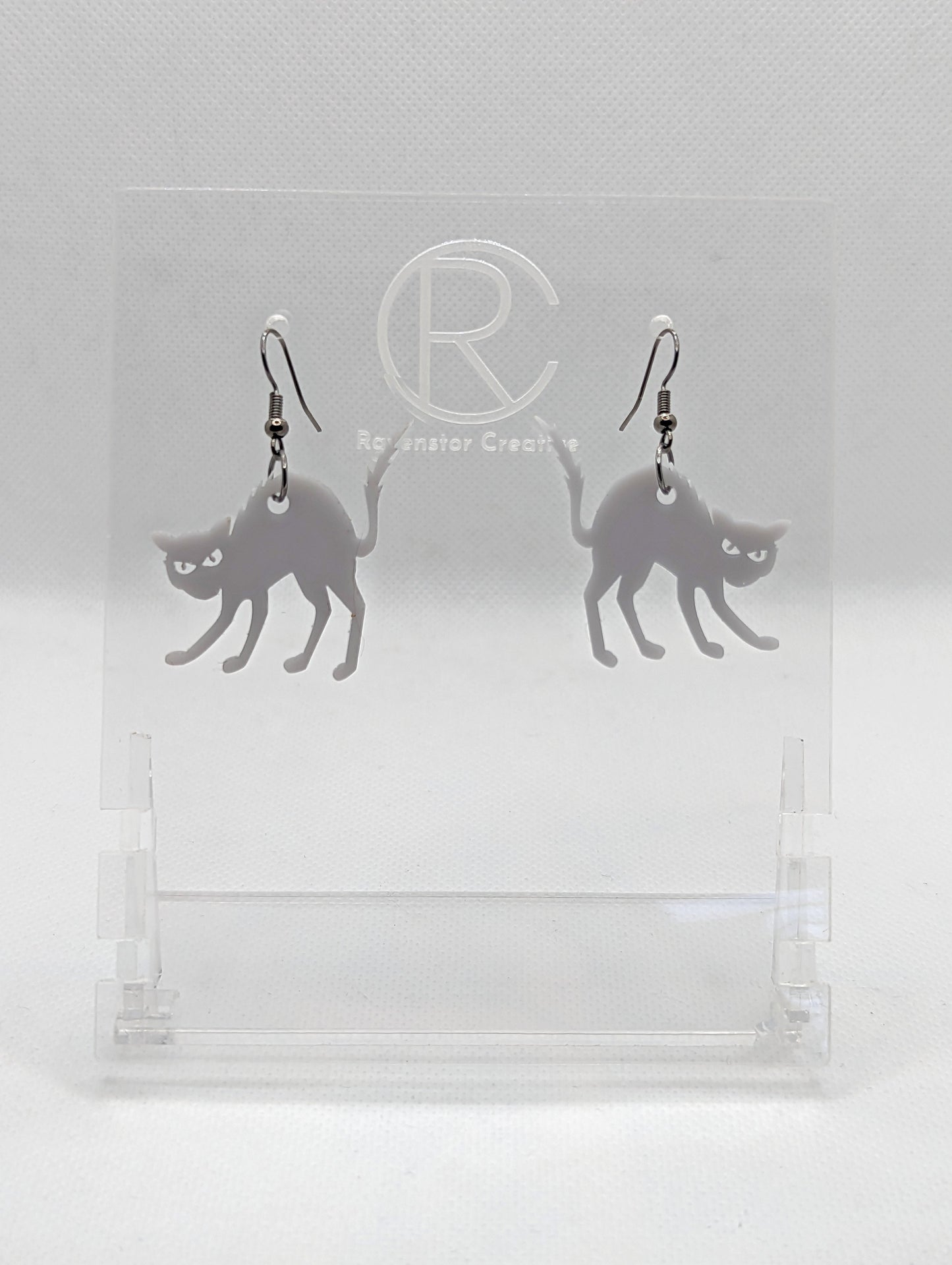 An image of a pair of earrings with black fixings on a white background, they are angry or scared looking cats in grey with thier heckles and tails up and fir on end. Great for Halloween