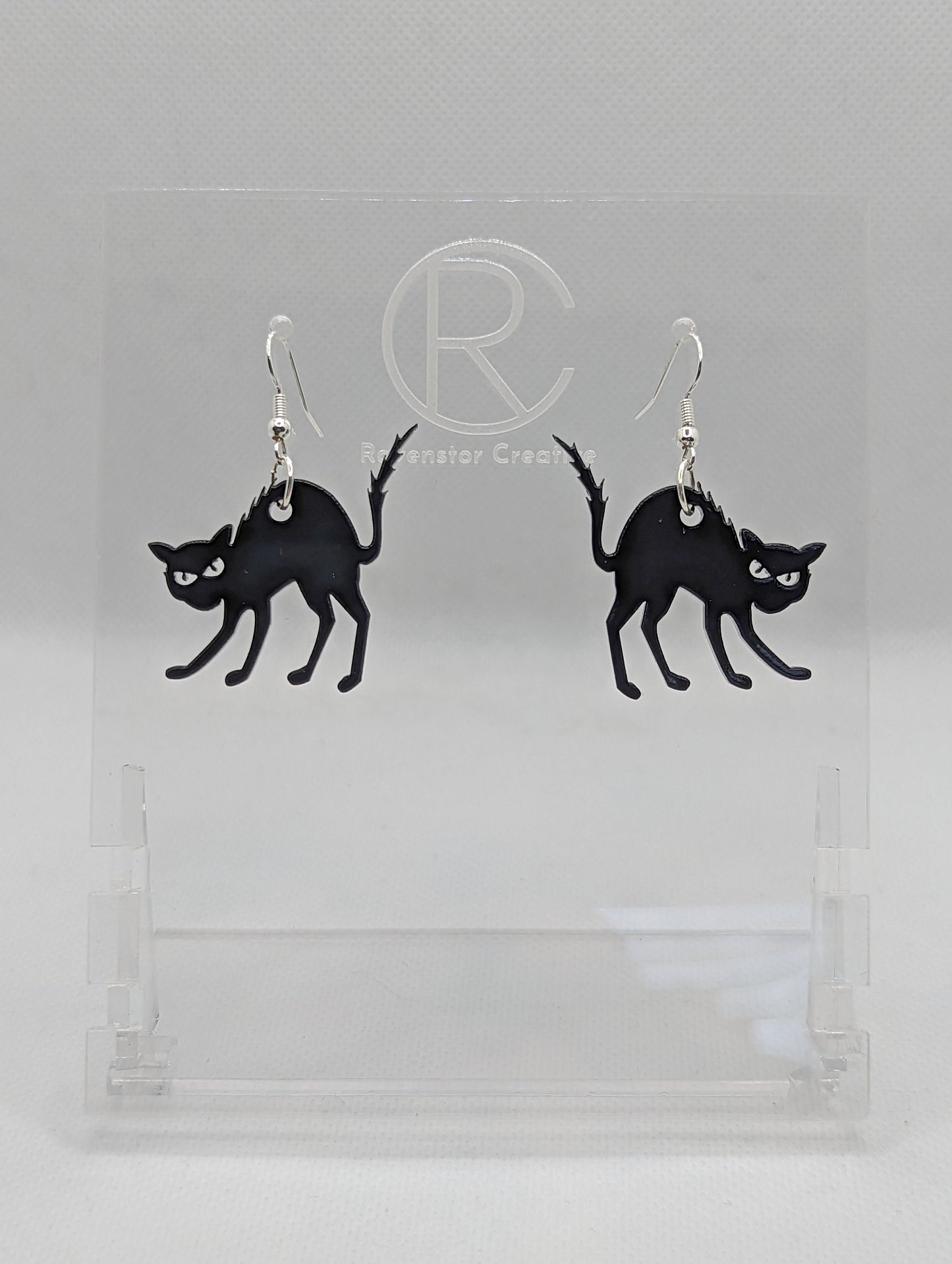 An image of a pair of earrings with silver fixings on a white background, they are angry or scared looking cats in black with thier heckles and tails up and fir on end. Great for Halloween