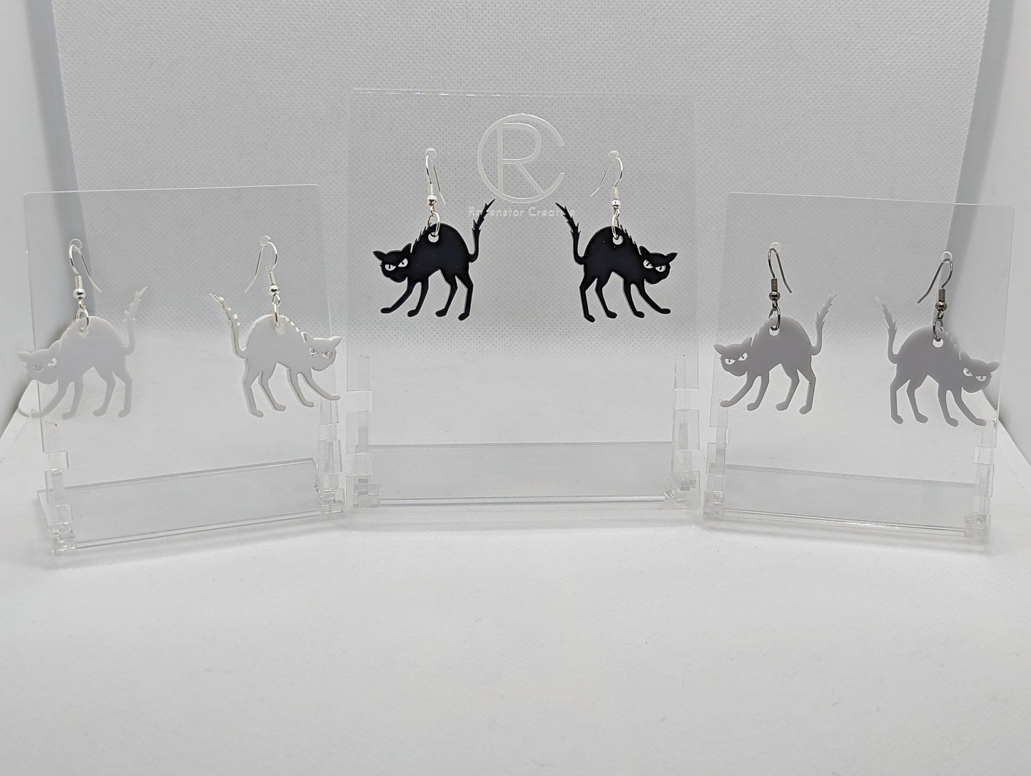 An image of 3 pairs of earrings with silver & black fixings on a white background, they are angry or scared looking cats with thier heckles and tails up and fir on end. The colours shown are Black, white and grey..