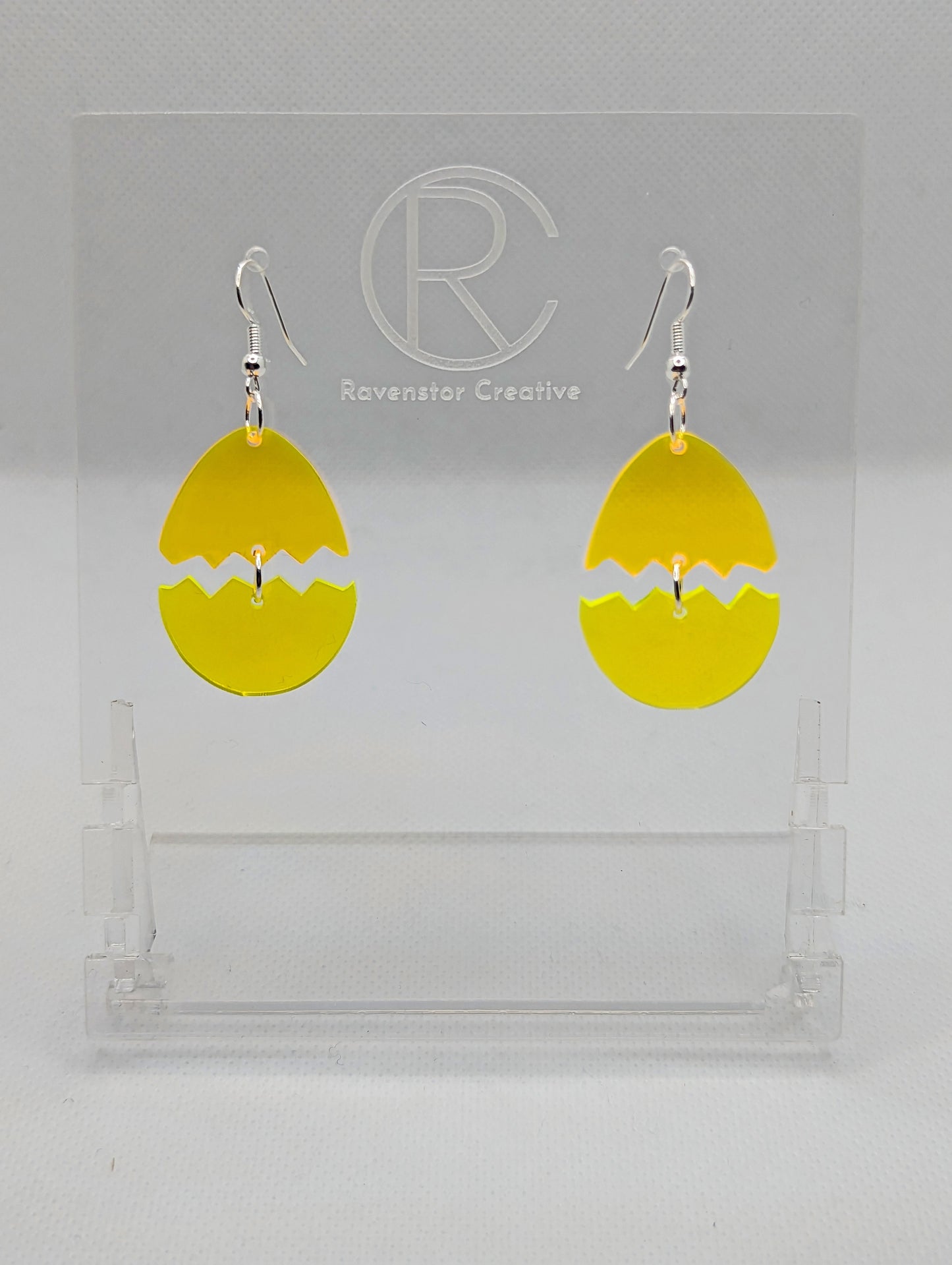 Shows a pair of Easter egg earrings cracked in the middle separating it into two parts. They have Silver ear wire hook fixings that attach to the top and the bottom dangles under. The colours are Neon Orange top and Neon Yellow bottom.