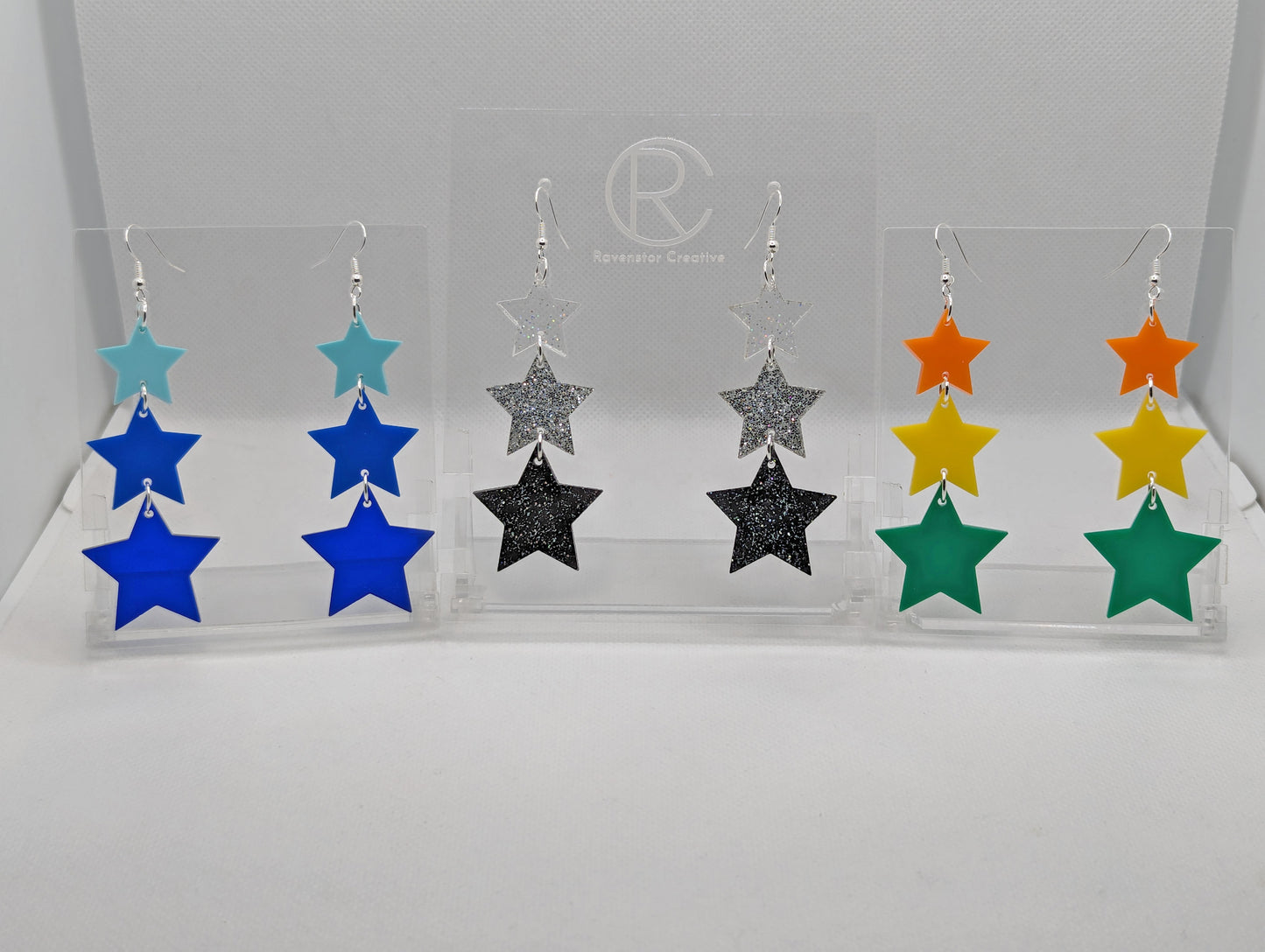 Three pairs of earrings, each has three stars dangling from each other, the top is the smallest and they get bigger as they go down. Colours are (from the top) Spearmint, Blue and trans Blue. Glitters clear, silver and black. orange, yellow and green