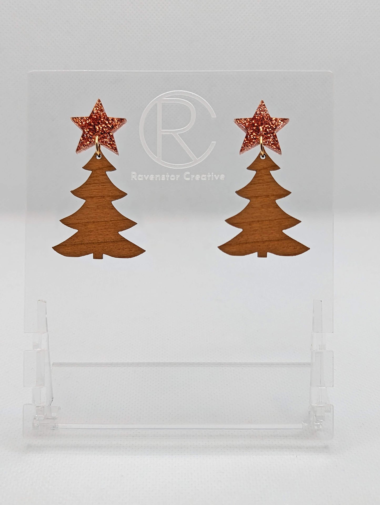 A pair of acrylic Christmas tree earrings in two parts that have stud fixings. The studs are attached to a star with the tree dangling under They have a Copper Glitter star with a Cherry Wood Christmas Tree Dangling underneath.