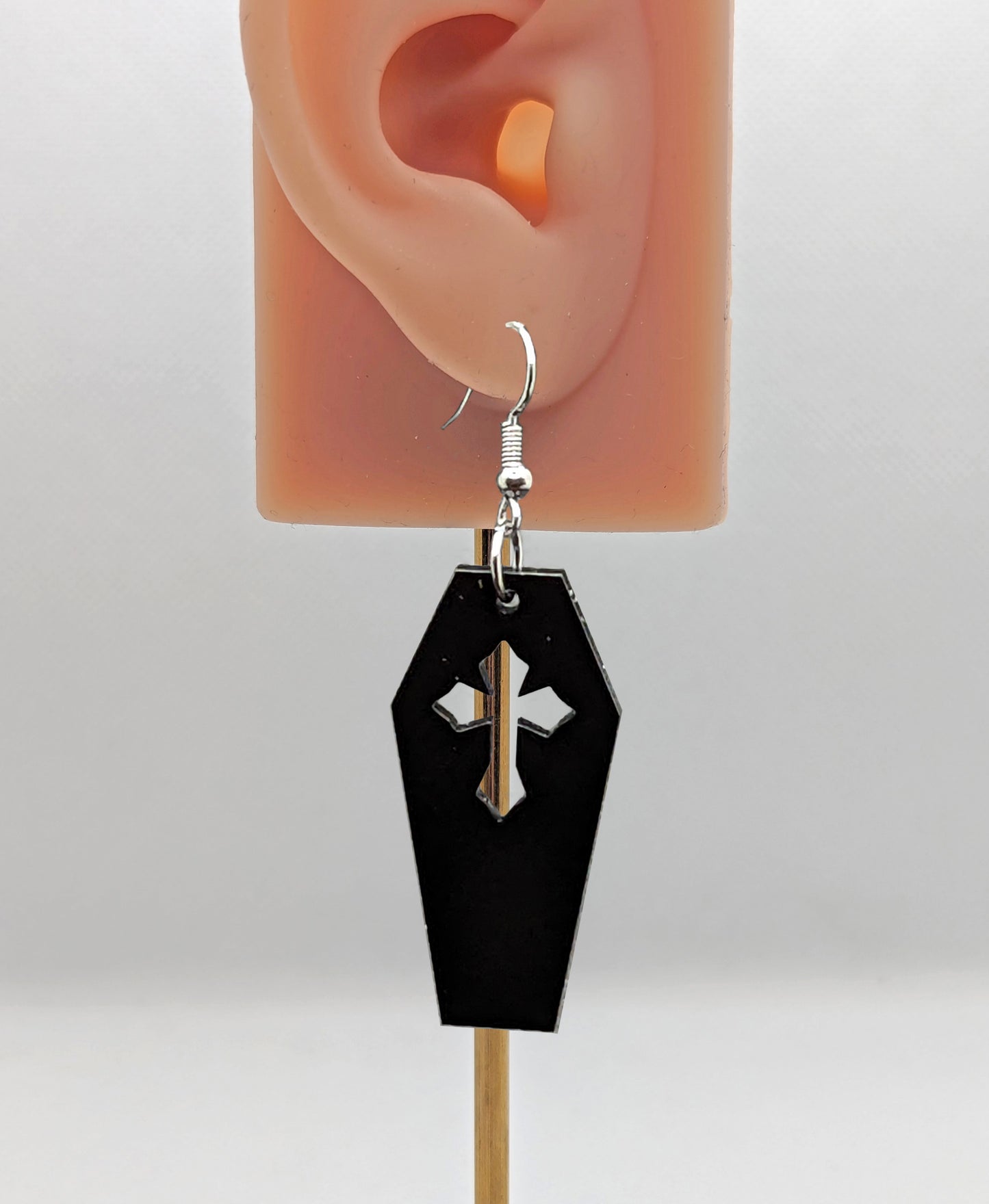 Image of a Halloween coffin / Casket shaped earring on an ear showing the size against a white background. It is made from black acrylic and have silver ear wire hook fixings.