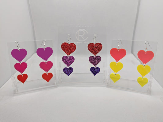 Three pairs of earrings, each has three hearts dangling from each other, the top is the biggest and they get smaller as they go down. Colours are (from the top) Grape, Hot pink and Red. Glitters Red, Pink and Purple. Neons Pink, Orange and yellow.