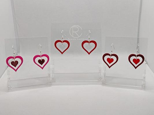 Shows three pairs earrings ear wire hook fixings. They are Heart shapes with a smaller heart dangling inside them. The colours are Hot pink outer with maroon inner, translucent red outer with clear inner and maroon outer and translucent red inner.