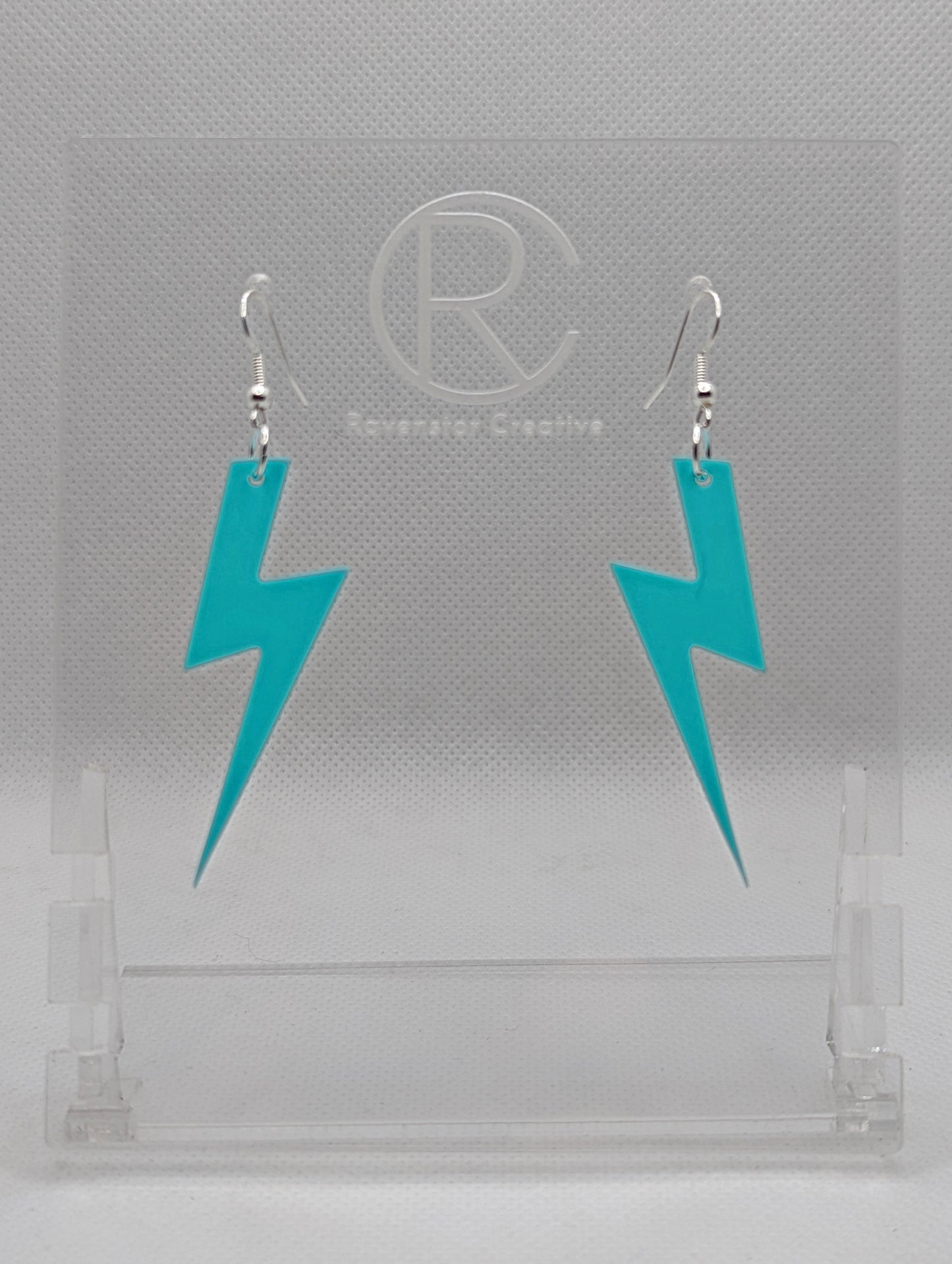 Shows a pair of acrylic earrings that have silver ear wire hook fixings. They are Lightning Bolt shapes similar to Harry Potter's forehead. They are spearmint colour and are against a white background on see through stand.