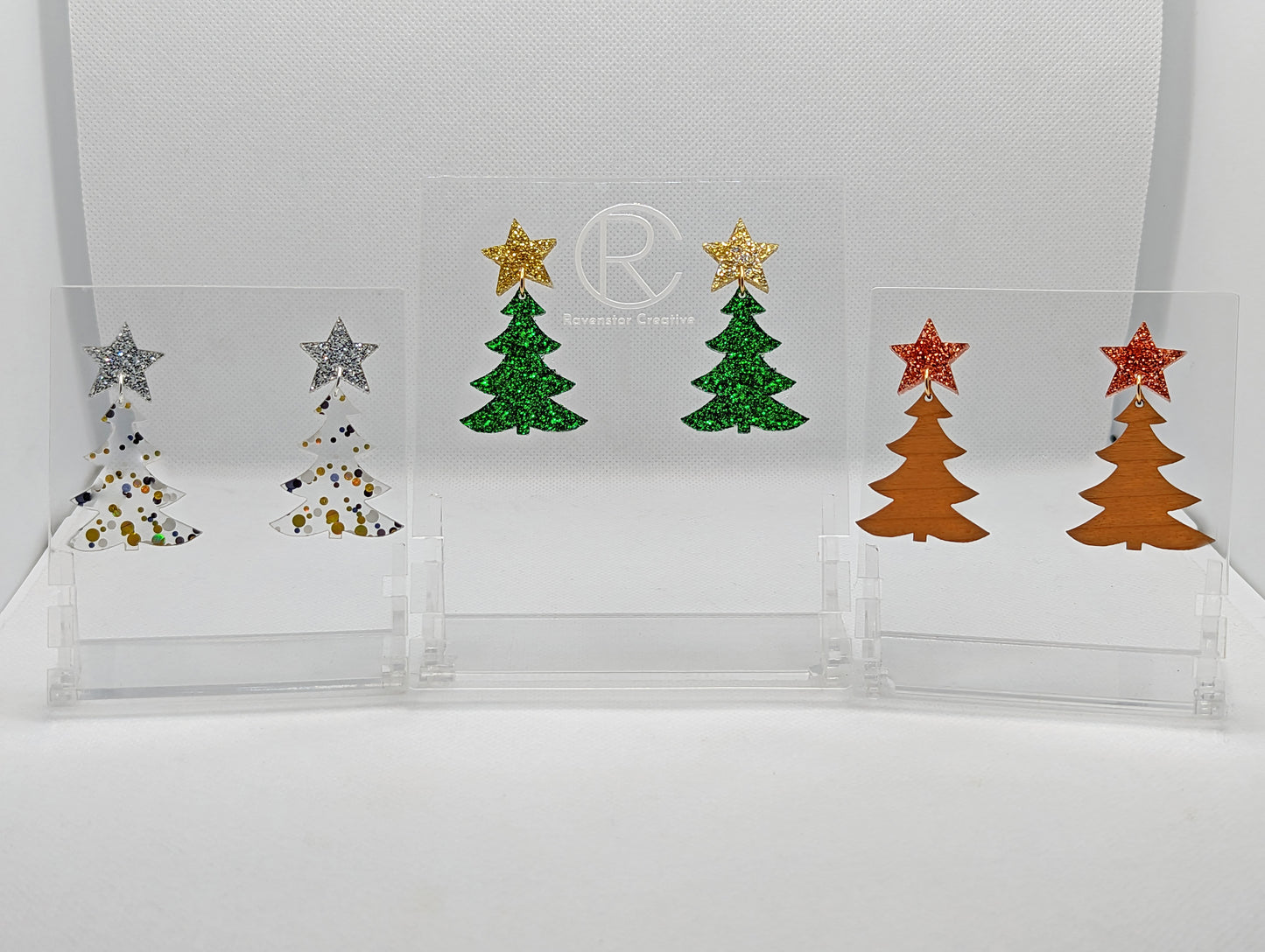 Three pairs of Christmas Tree earrings in two parts that have stud fixings. The studs are attached to a star with the tree dangling under. The colours are Silver and Lollipop glitter. Gold Glitter with Green Glitter. Copper Glitter with Cherry wood.
