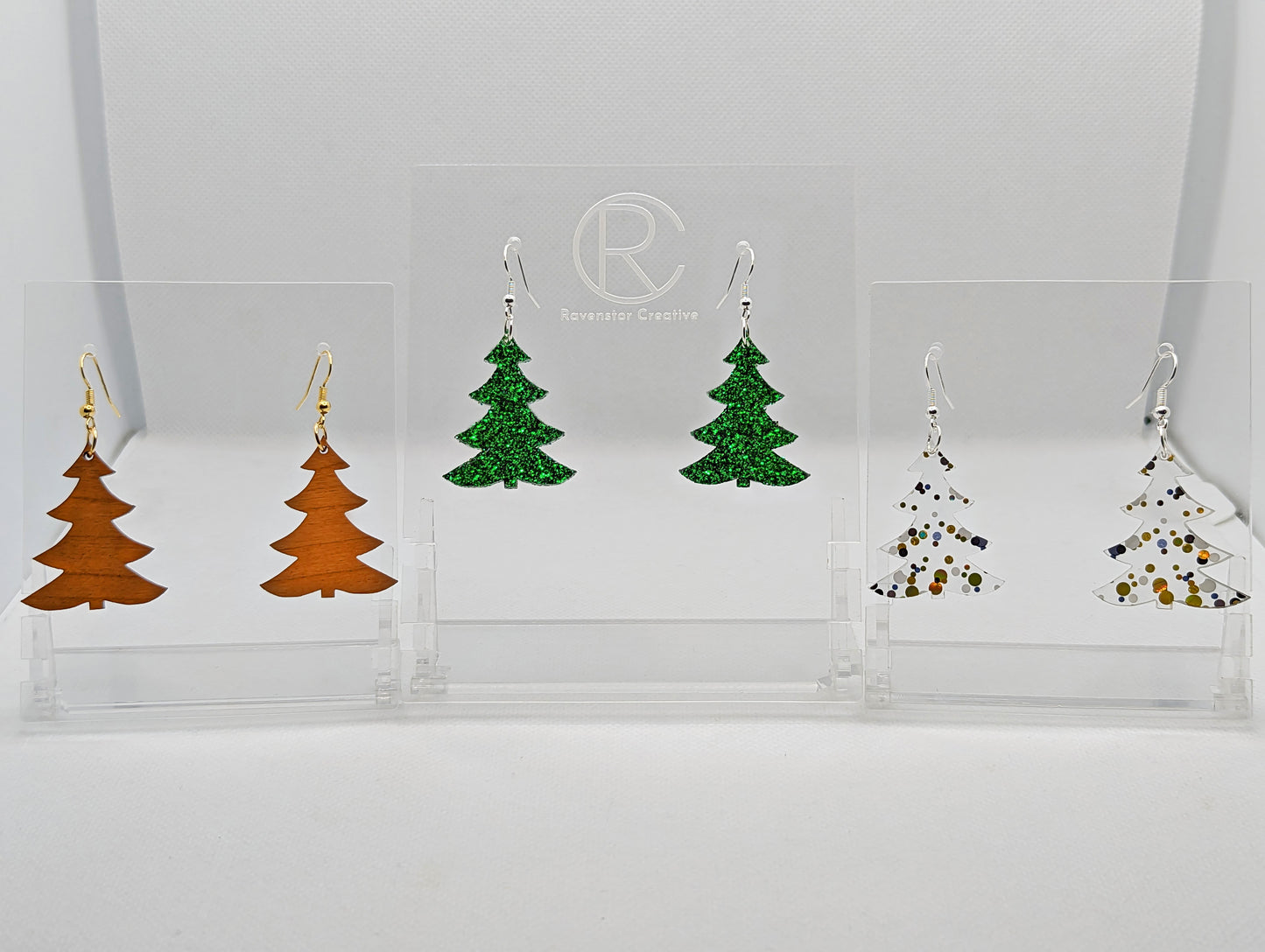 Image showing three pairs for earrings with ear wire hook fixings. They are Christmas / Xmas Tree shapes. The colours are Cherry Wood with Gold fixings, Green Glitter with silver fixings and Lollipop Glitter with Silver fixings.