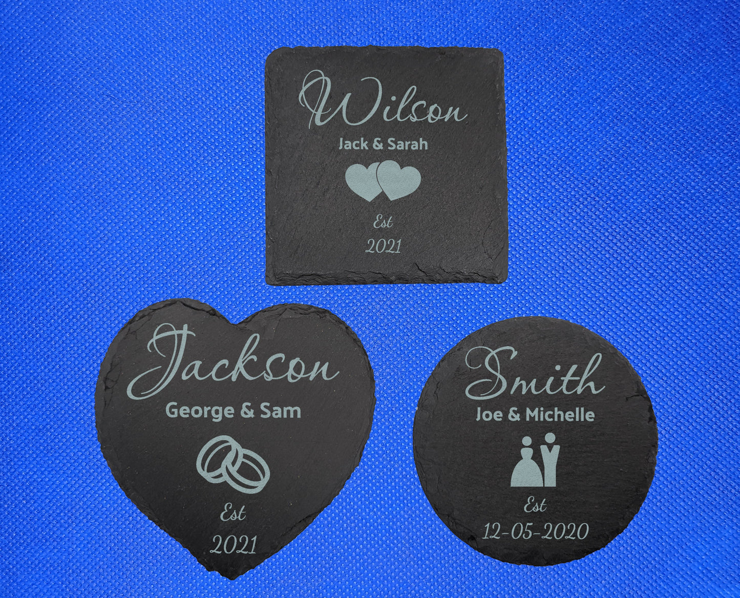 3 Slate coasters engraved with example Wedding themes. The square says Wilson Jack and Sarah Est 2021 with heart image. Heart has Jackson George and Sam Est 2021 with ring image and circle has Smith Joe and Michelle Est 12.05.2020 with couple image