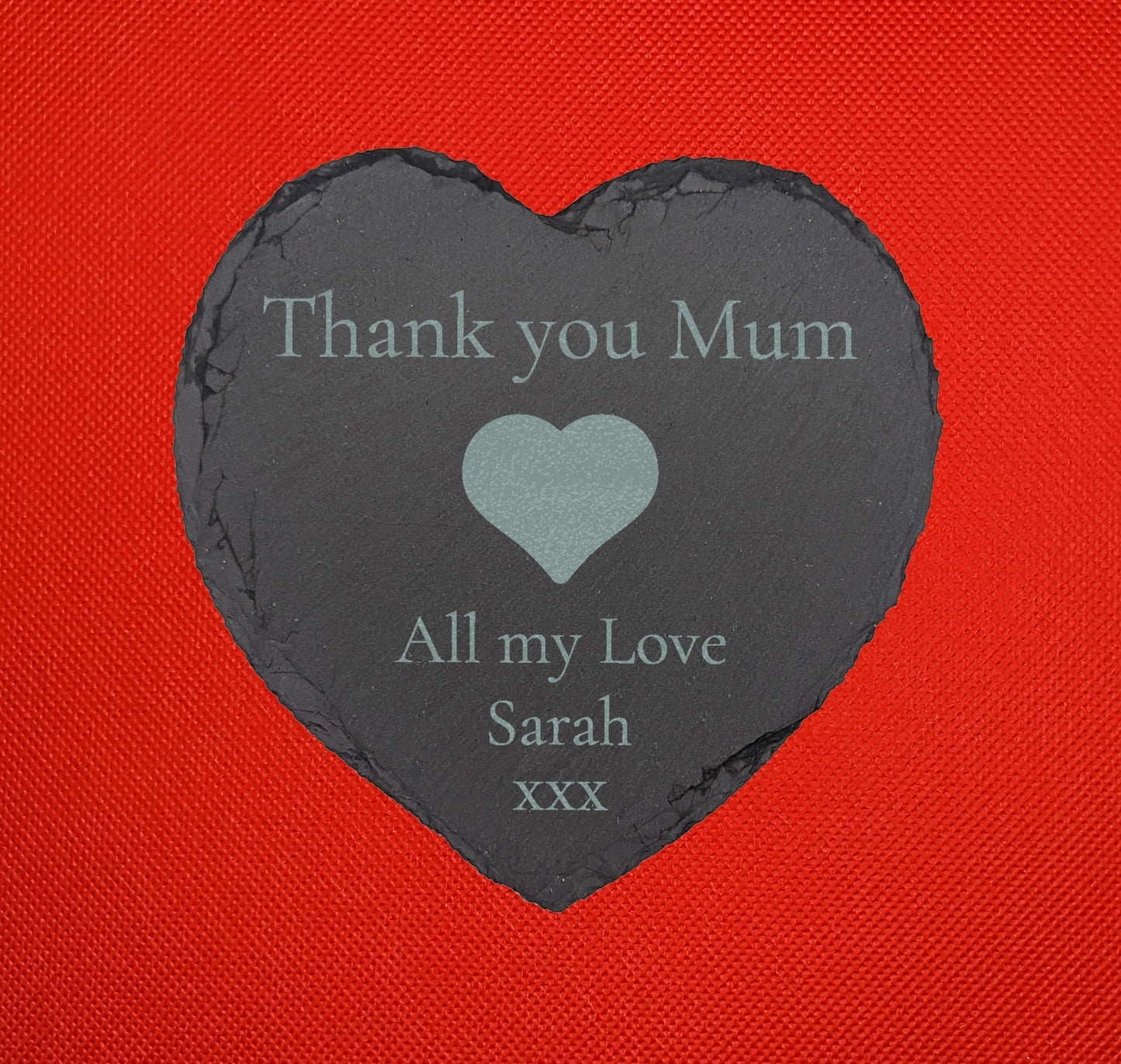 Shows a mum themed slate heart coaster 10cm by 10cm. It is engraved with example text saying Thank you Mum All my Love Sarah xxx with an image a Heart in the middle. It is against a Red background.