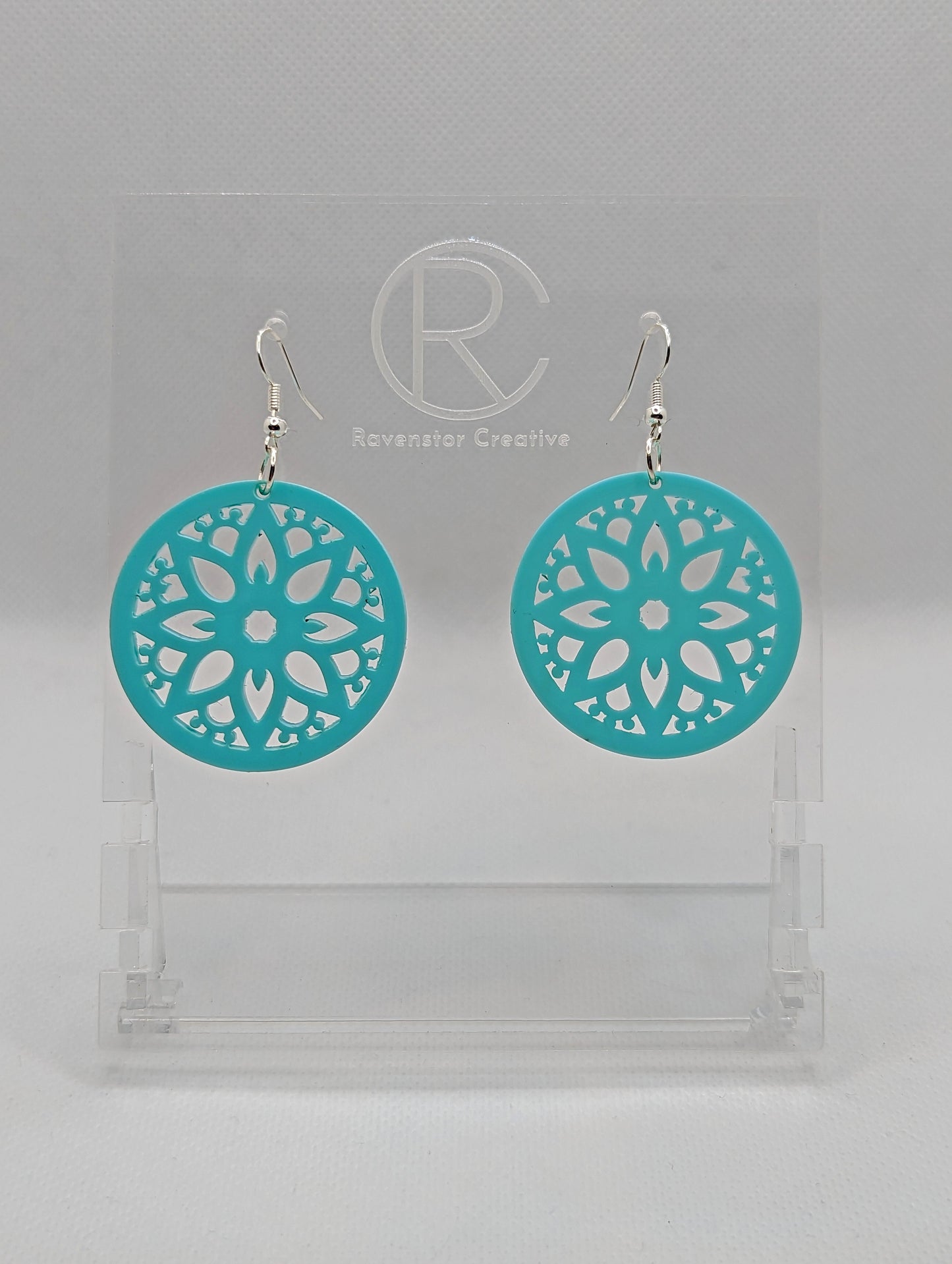Shows a pair of acrylic earrings that have silver ear wire hook fixings. They are Floral Themed Circle earrings with an intricate pattern cut out of the middle. They are spearmint in colour and are against a white background on see through stand.