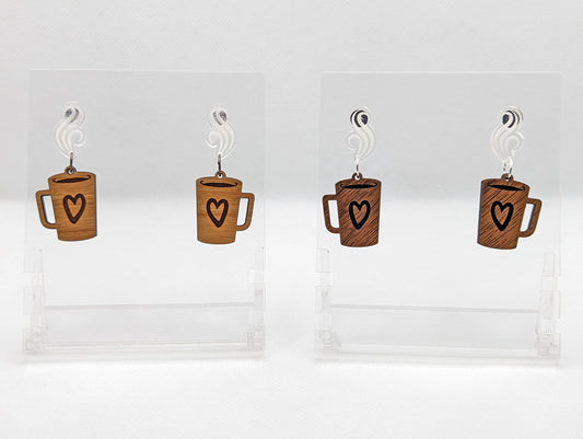 Shows 2 pairs of earrings that are two parts. Stud fixings are attached to a clear acrylic steam shape, dangling under are Coffee mugs / cups with a heart engraved on them. The left pair are Cherry wood and right pair are Walnut wood.