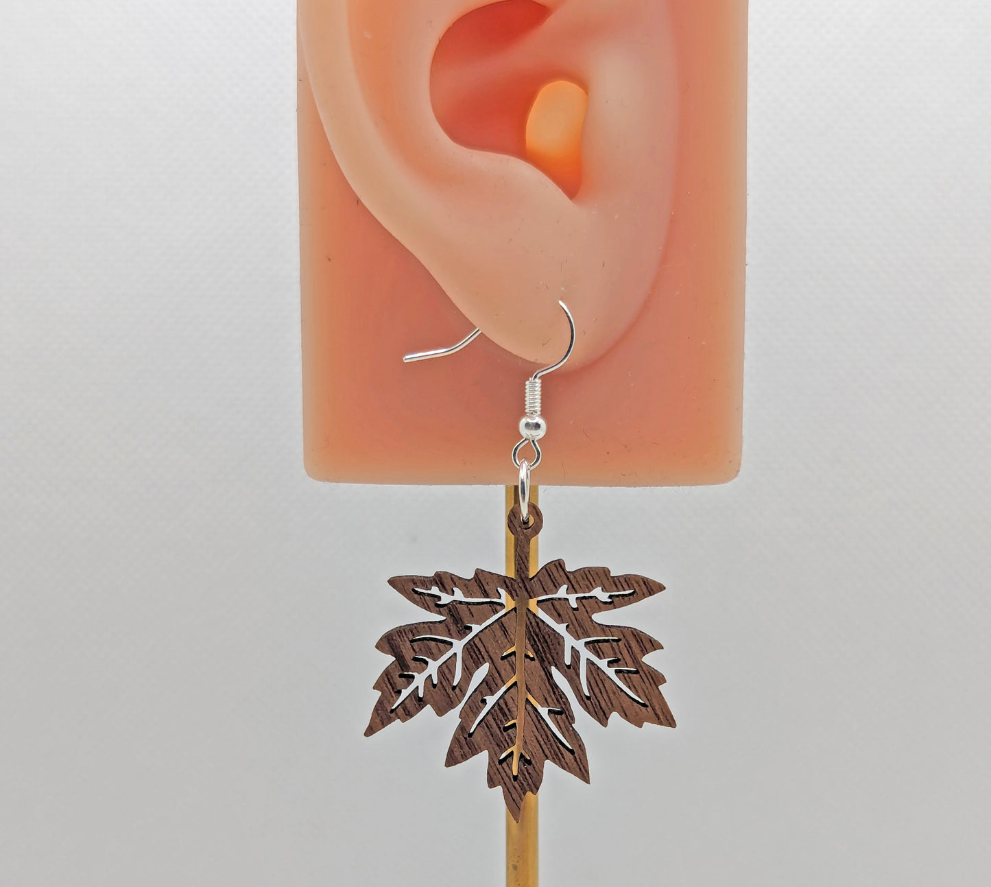 Image of a pair of Autumn Fall Maple Leaves on an ear showing the size against a white background. They are walnut wood and have silver fixings.