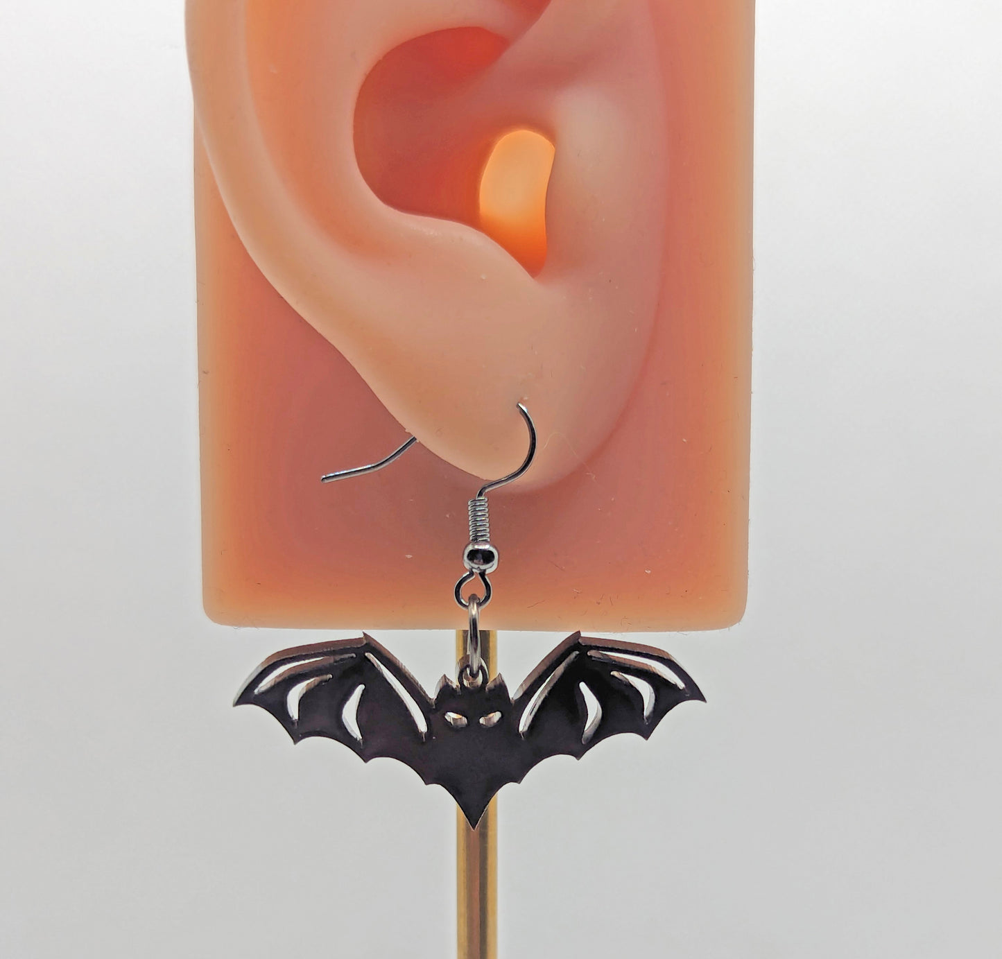 Image of a pair of Halloween Bat shaped earrings on an ear showing the size against a white background. They are black and have black fixings.