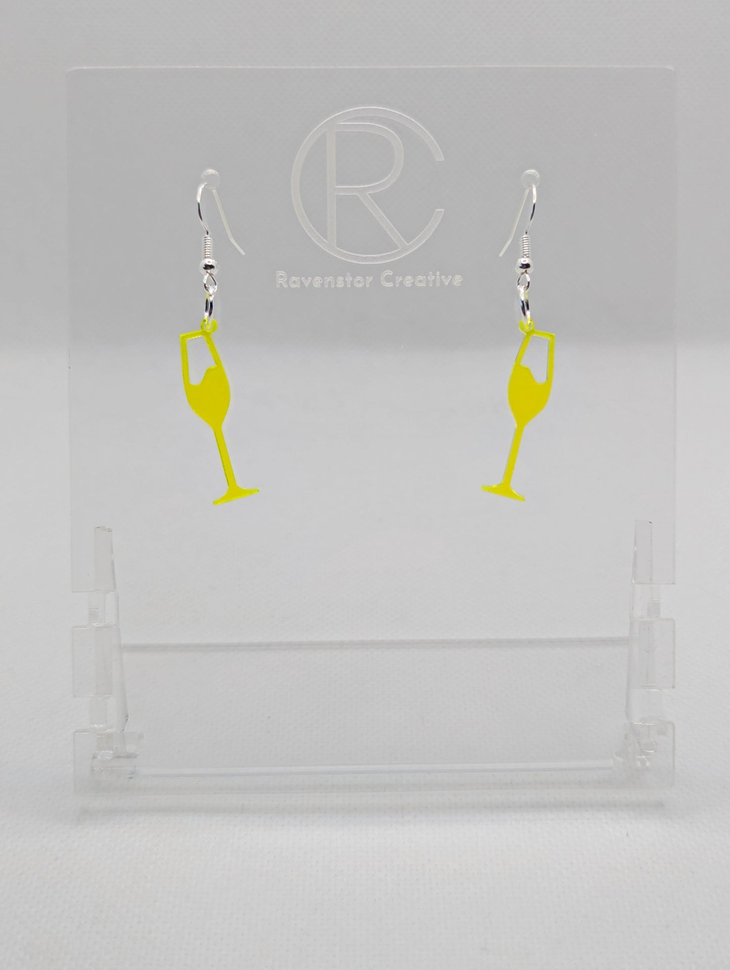 An image of a pair of Champaign Glass Earrings with Silver ear wire hook fixings. These are ideal for a Hen Do or Bachelorette Party. The colour is Neon Orange. They are on clear stands against a white background.