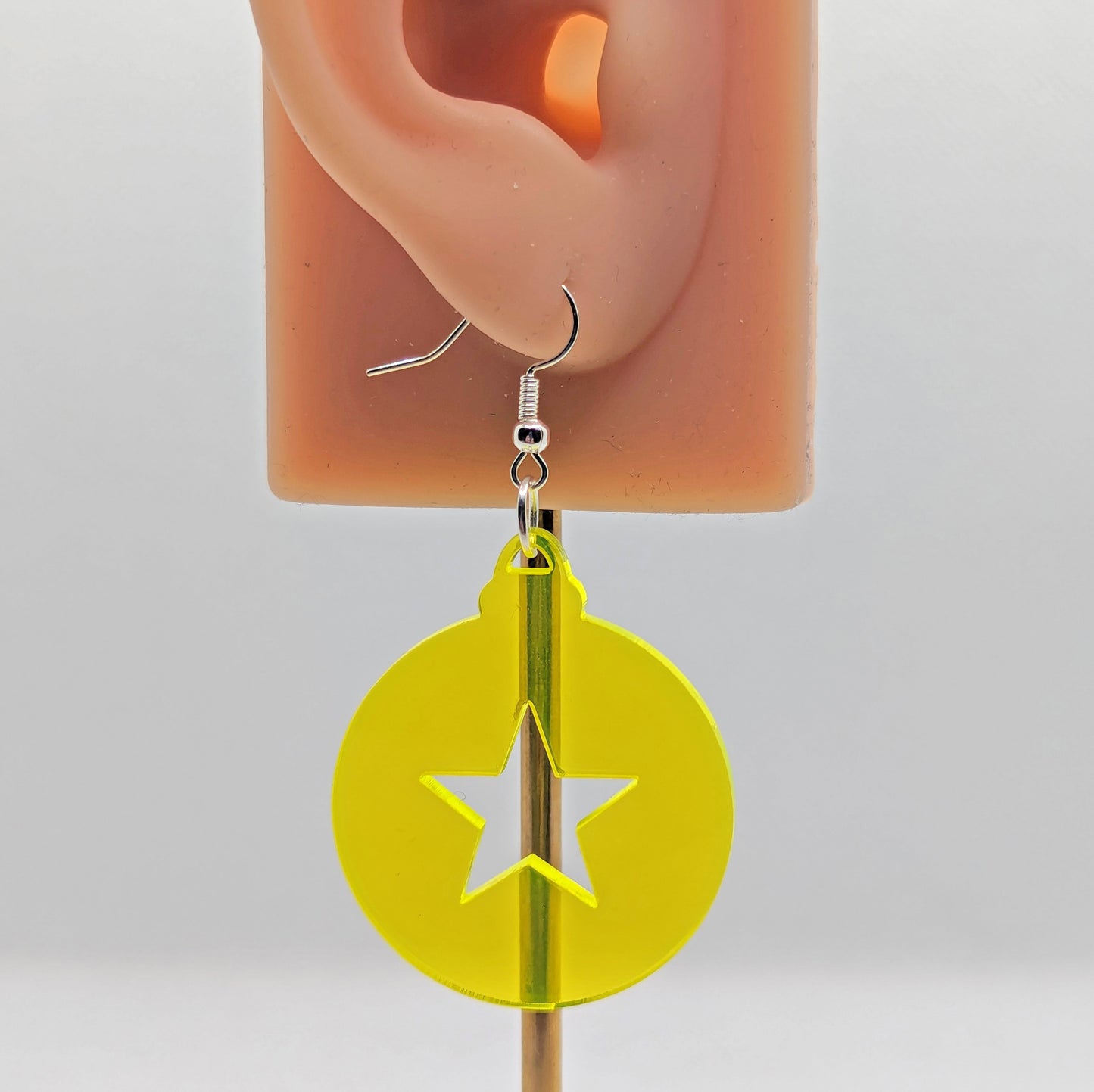 Image of a pair of earrings. They are Christmas / Xmas bauble shapes with a star cut out in Neon Yellow on an ear showing the size against a white background. They and have silver fixings.