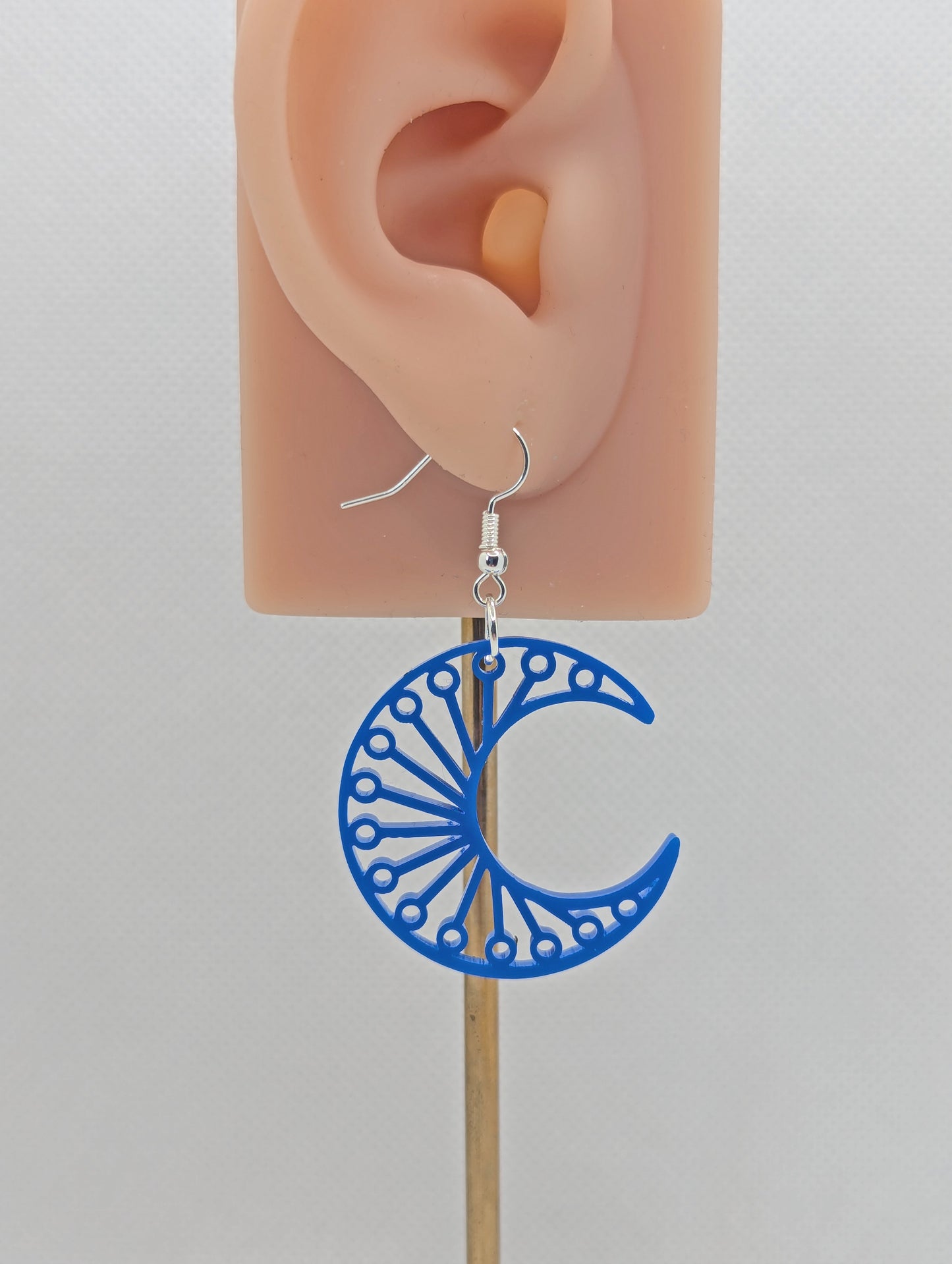 Shows an earrings that has a Silver ear wire hook fixing. it is a Decorative Crescent Moon earring. The colour of them is Blue. They are on an ear to show the size against a white background.