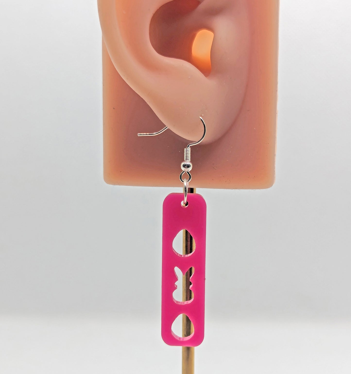A pair of earrings that have silver ear wire fixings. They are slim long bar pendant earrings with three Easter egg and rabbit / bunny shapes cut out. They are on an ear showing the size.