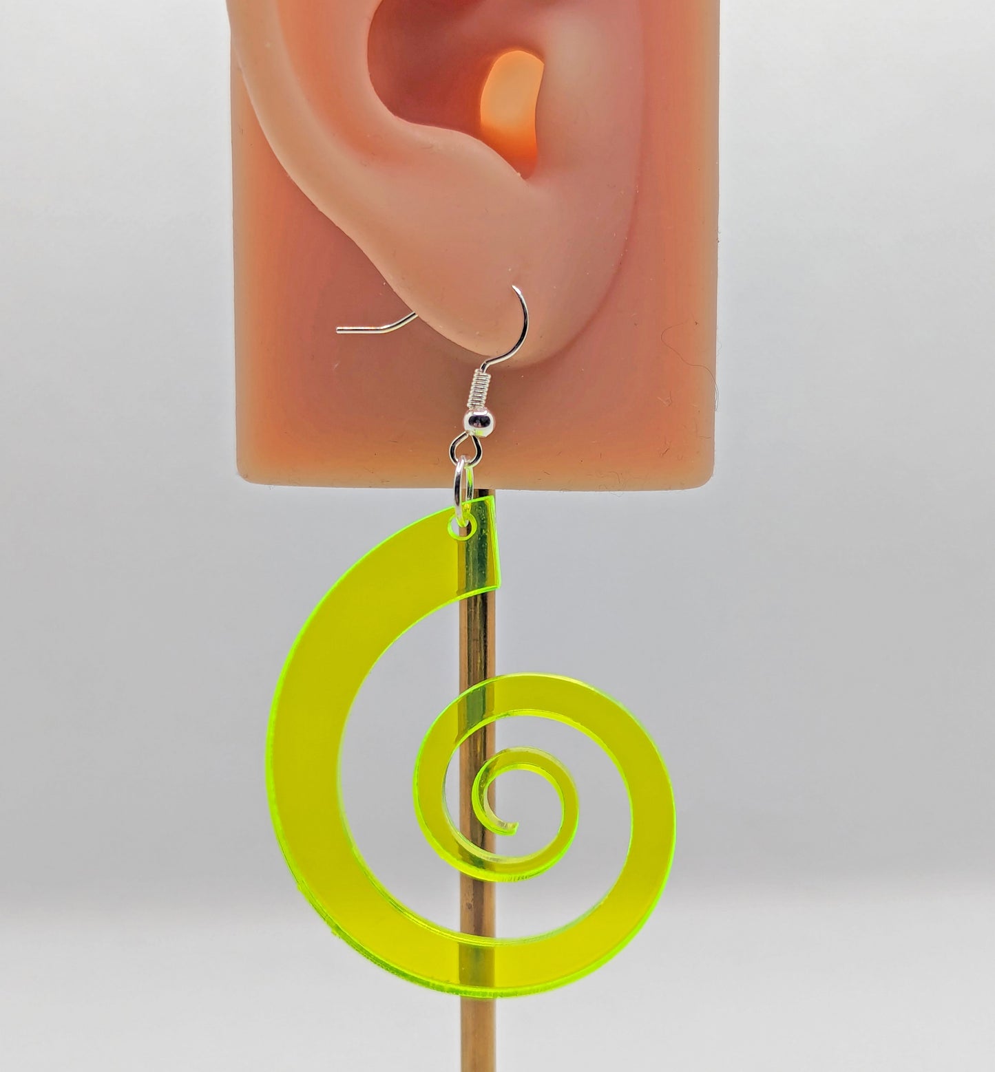 An earring on an ear showing the size. Retro 80s inspired spiral earring with silver ear wire hook fixings. It is made from Neon Green acrylic and is against a white background.