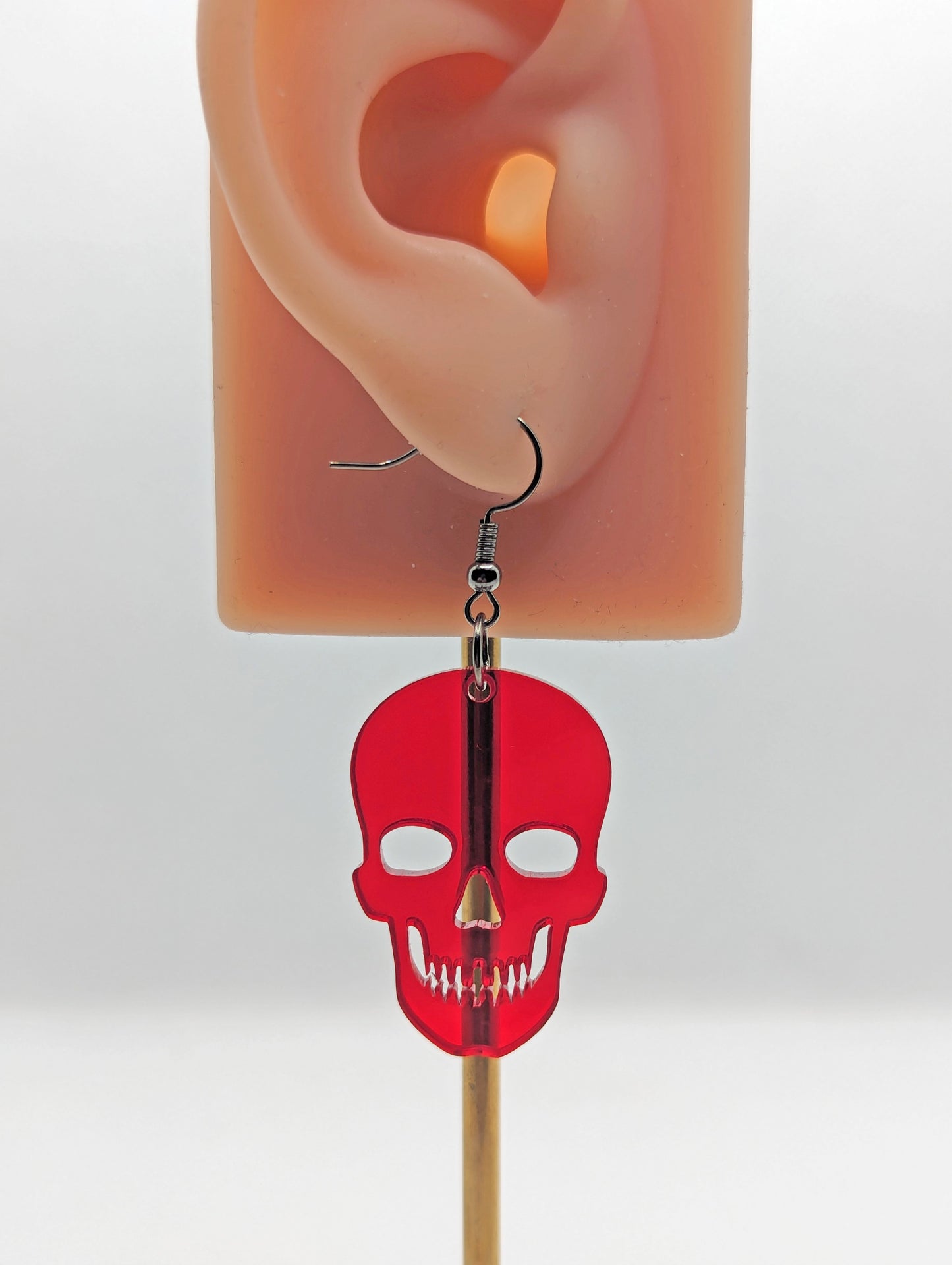 Image of a Halloween Skull shaped earring on an ear showing the size against a white background. It is made from translucent red acrylic and have black ear wire hook fixings.