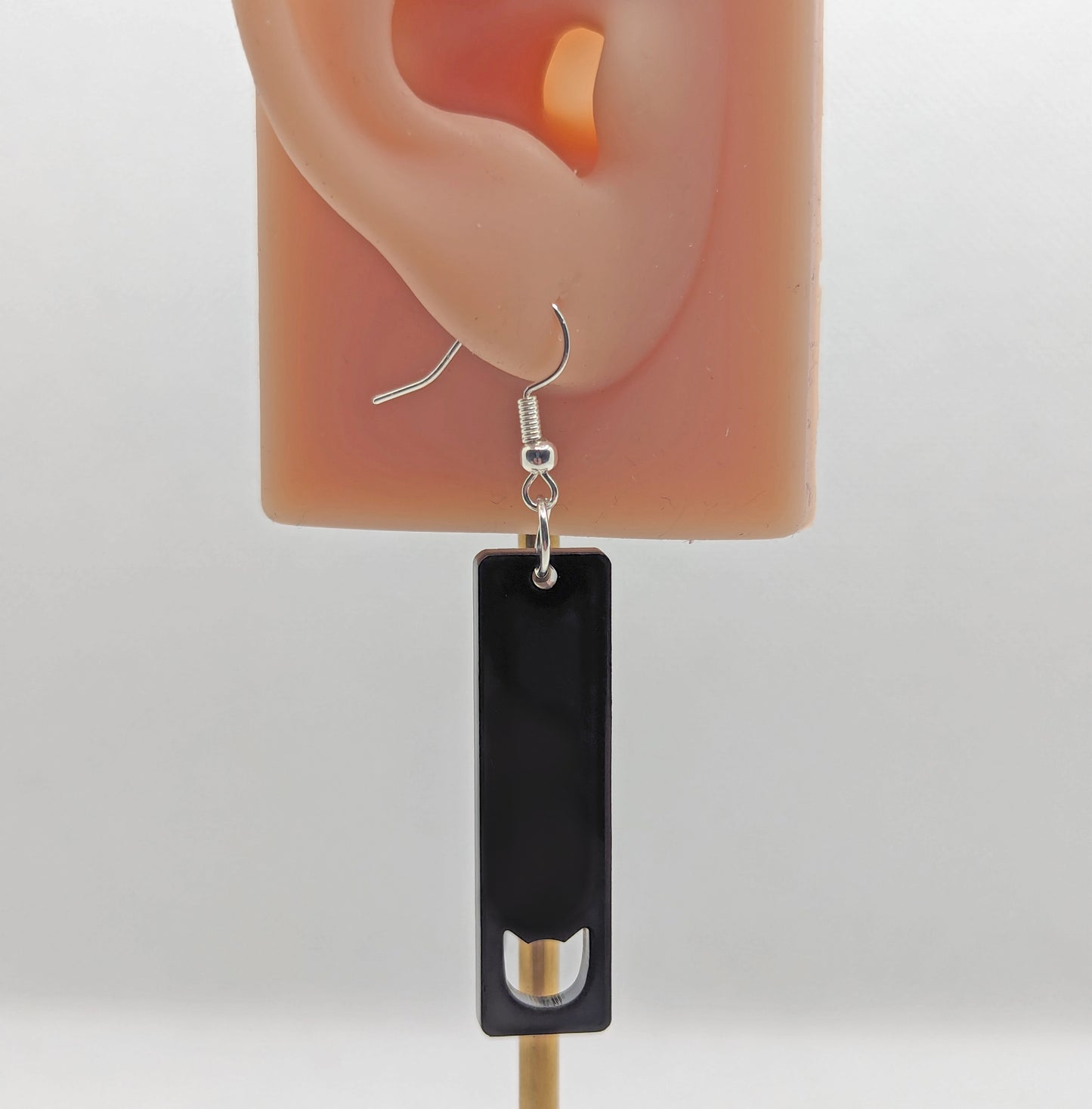 Image of a slim cat pendant earring on an ear showing the size against a white background. They are black and have silver ear wire hook fixings.