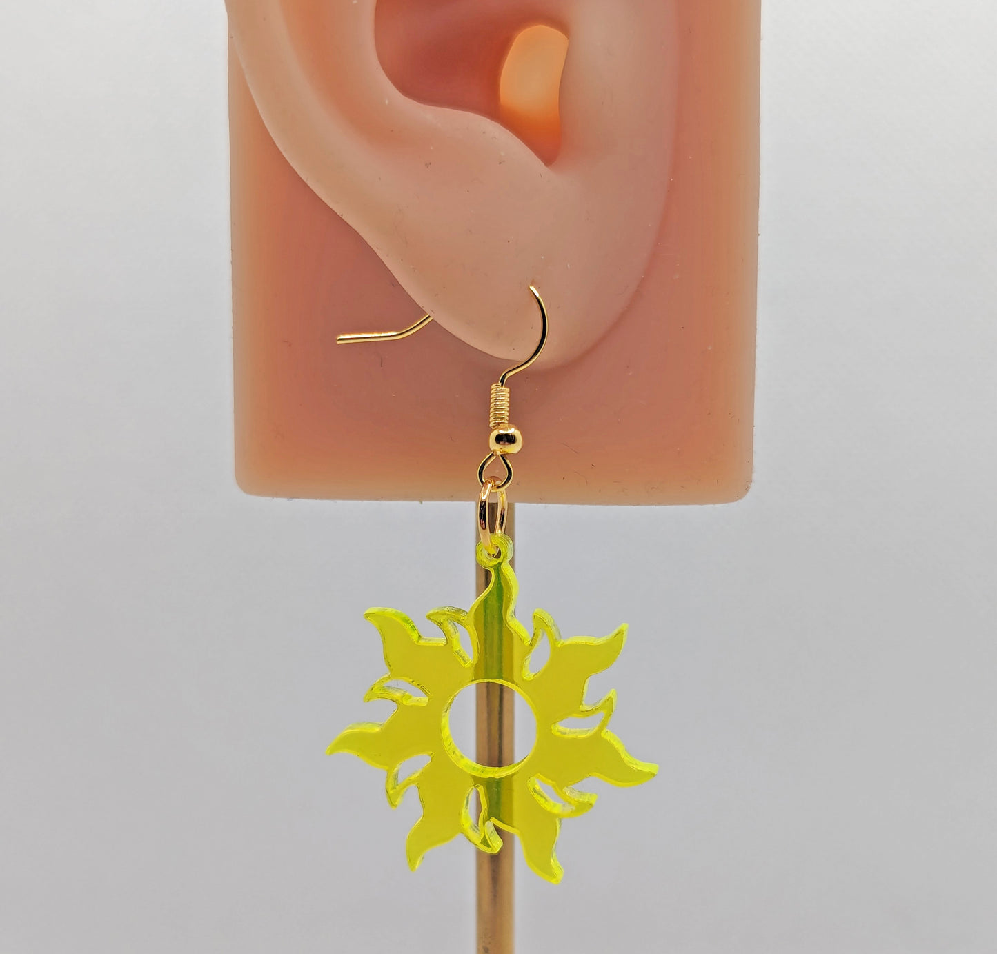 Image of a Shining Tangled Sun shaped earring on an ear showing the size against a white background. It is made from neon yellow acrylic and have gold ear wire hook fixings.