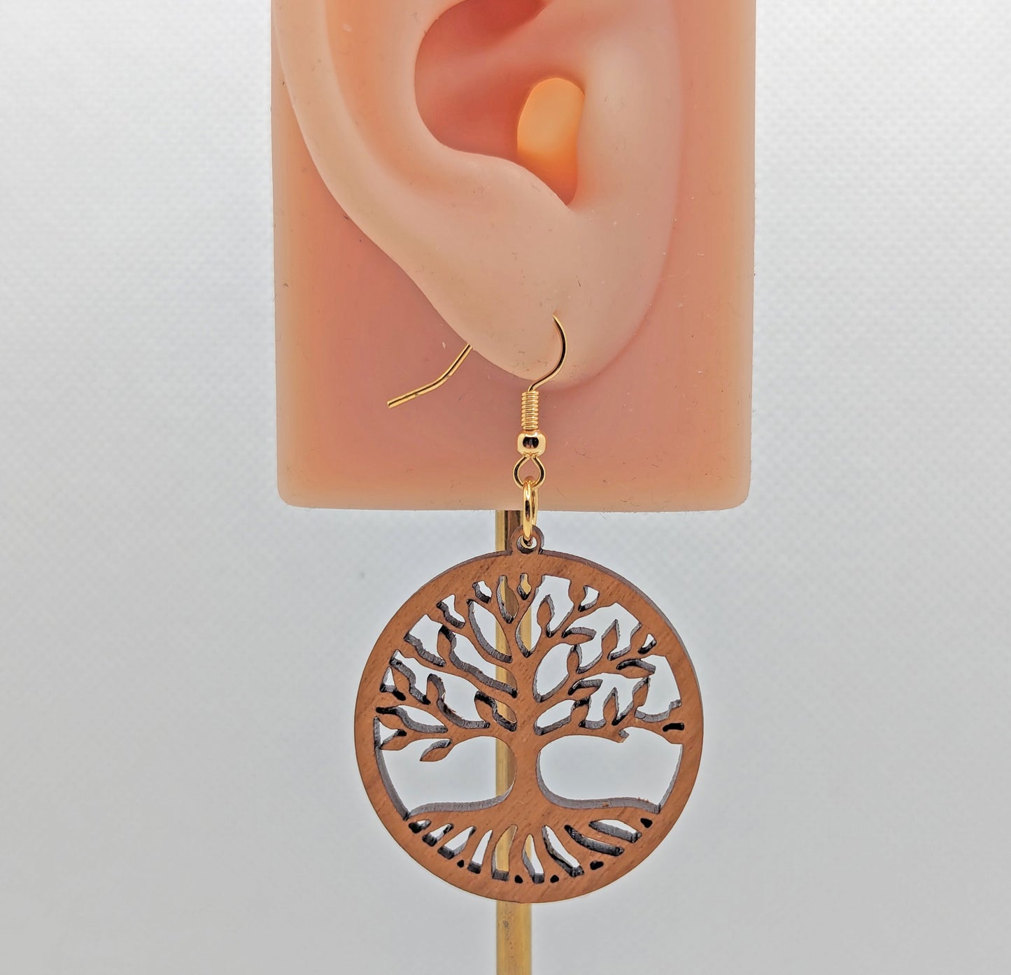 Image of a circle earrings with the tree of life cut out on an ear showing the size against a white background. It is made from cherry wood and have gold ear wire hook fixings.
