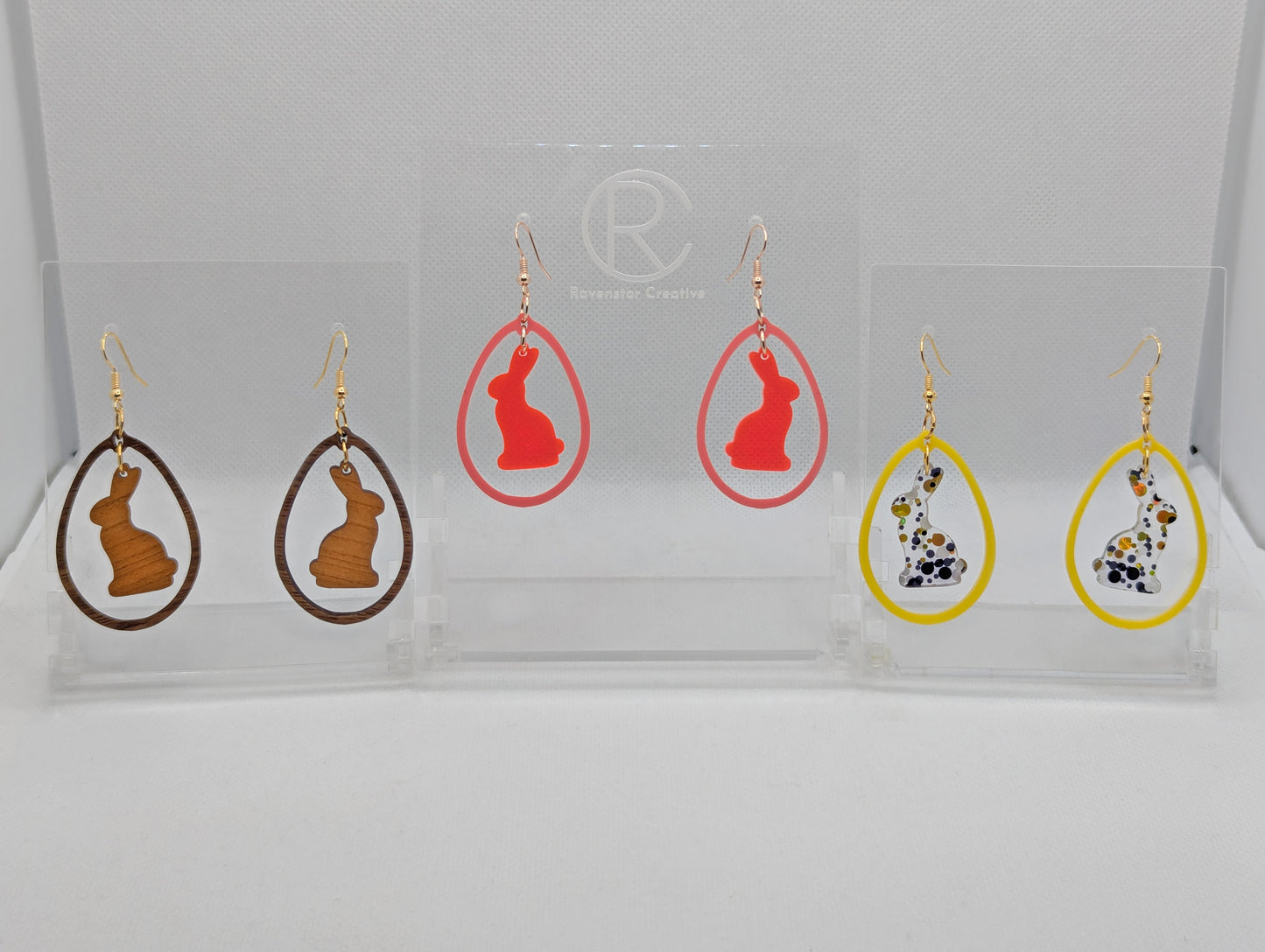 Three pairs of two part drop earrings with ear wire hook fixings. They are an egg shaped frame with a Bunny Rabbit dangling inside. The colours are Cherry Wood Bunny and Walnut Wood Egg, Neon Pink Bunny Sherbet Pink Egg, Lollipop Glitter and Yellow.