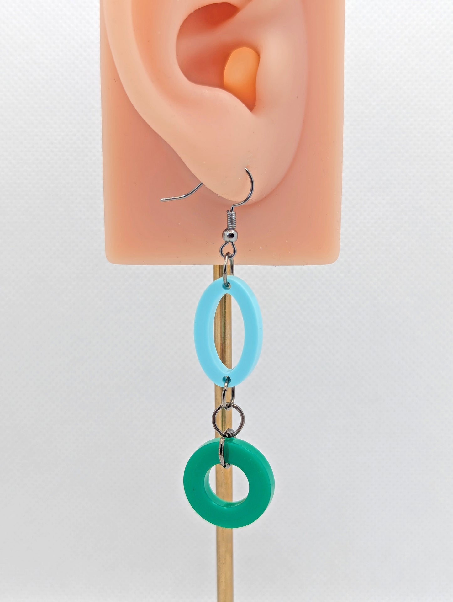 A two part drop earring with a Black ear wire hook fixing. It is an oval with a circle dangling underneath joined by three Black jump rings. The colours are Spearmint for the oval and Green for the circle. it is on an ear to show the size.