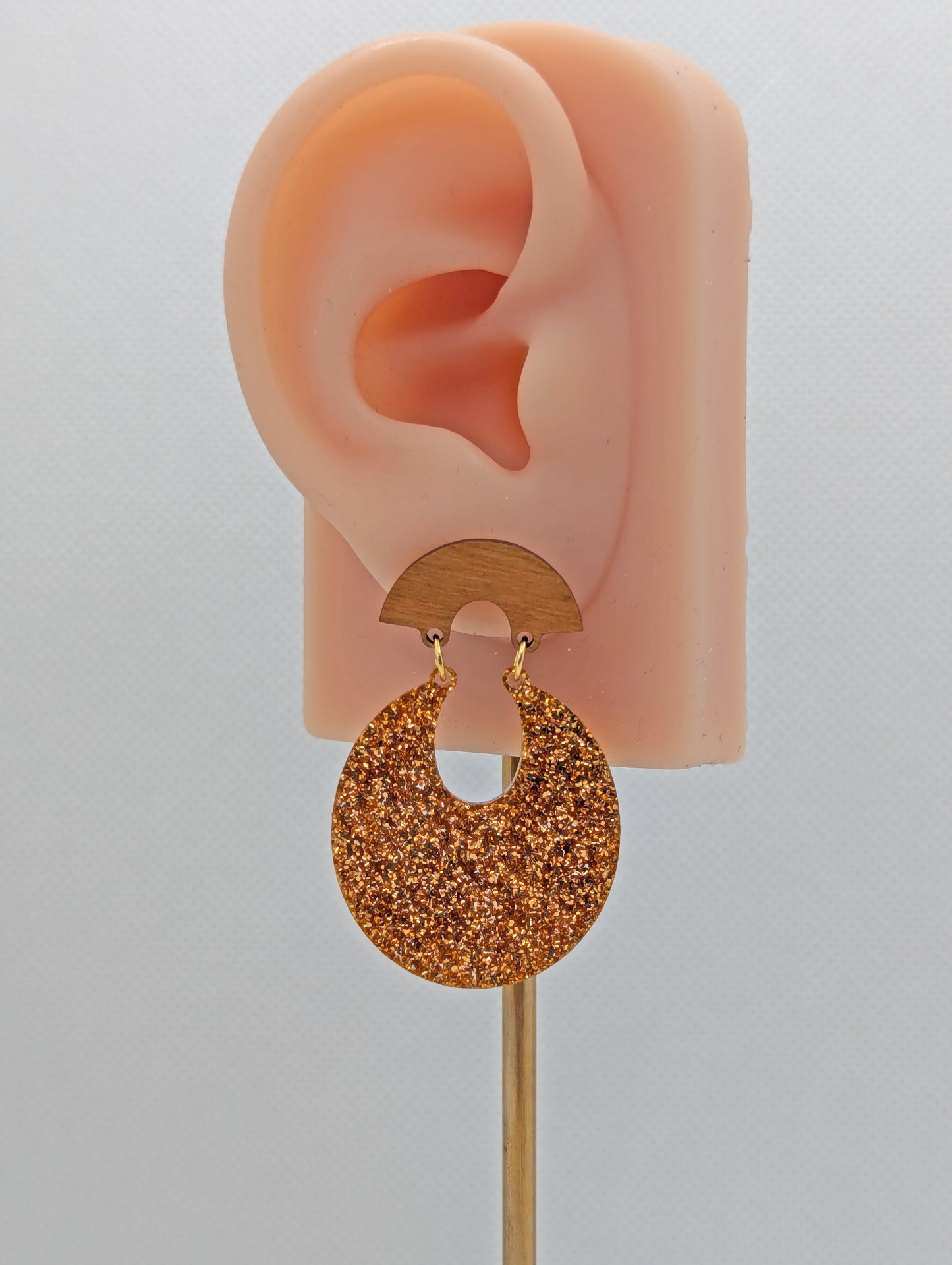 A pair of acrylic stud earrings. They are a small fan shape with an open hoop dangling underneath. The top fan is Cherry Wood and bottom part is an open hoop shape and is Copper Glitter. They are on an ear to show the size.