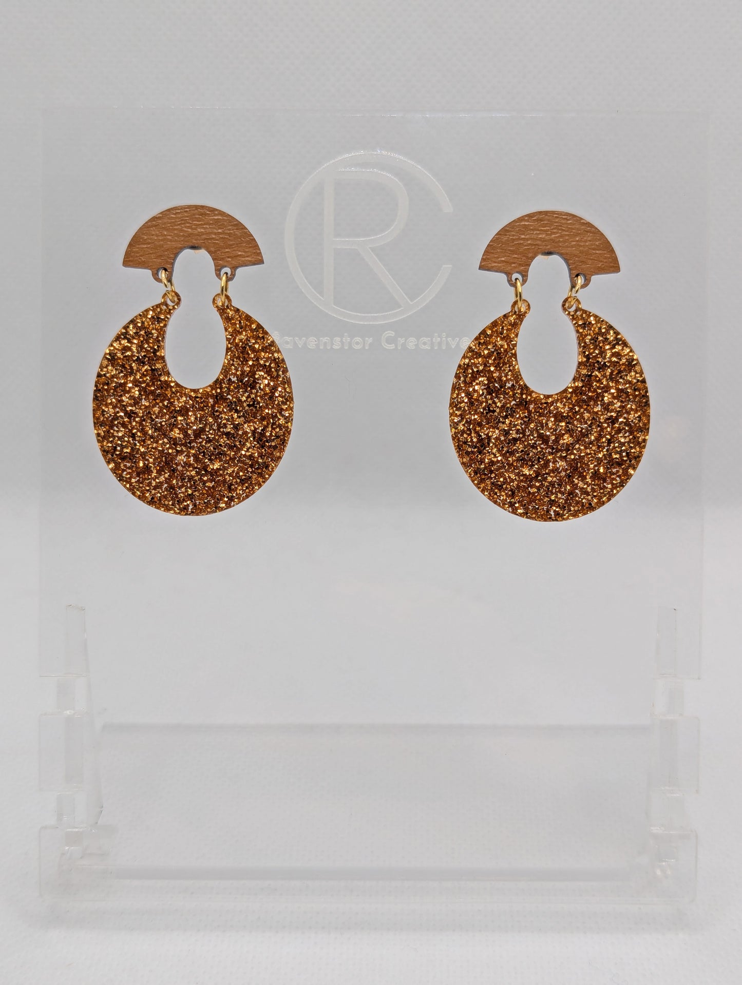 A pair of acrylic stud earrings. They are a small fan shape with an open hoop dangling underneath. The top fan is Cherry Wood and bottom part is an open hoop shape and is Copper Glitter. They are on a clear stand against a white background.