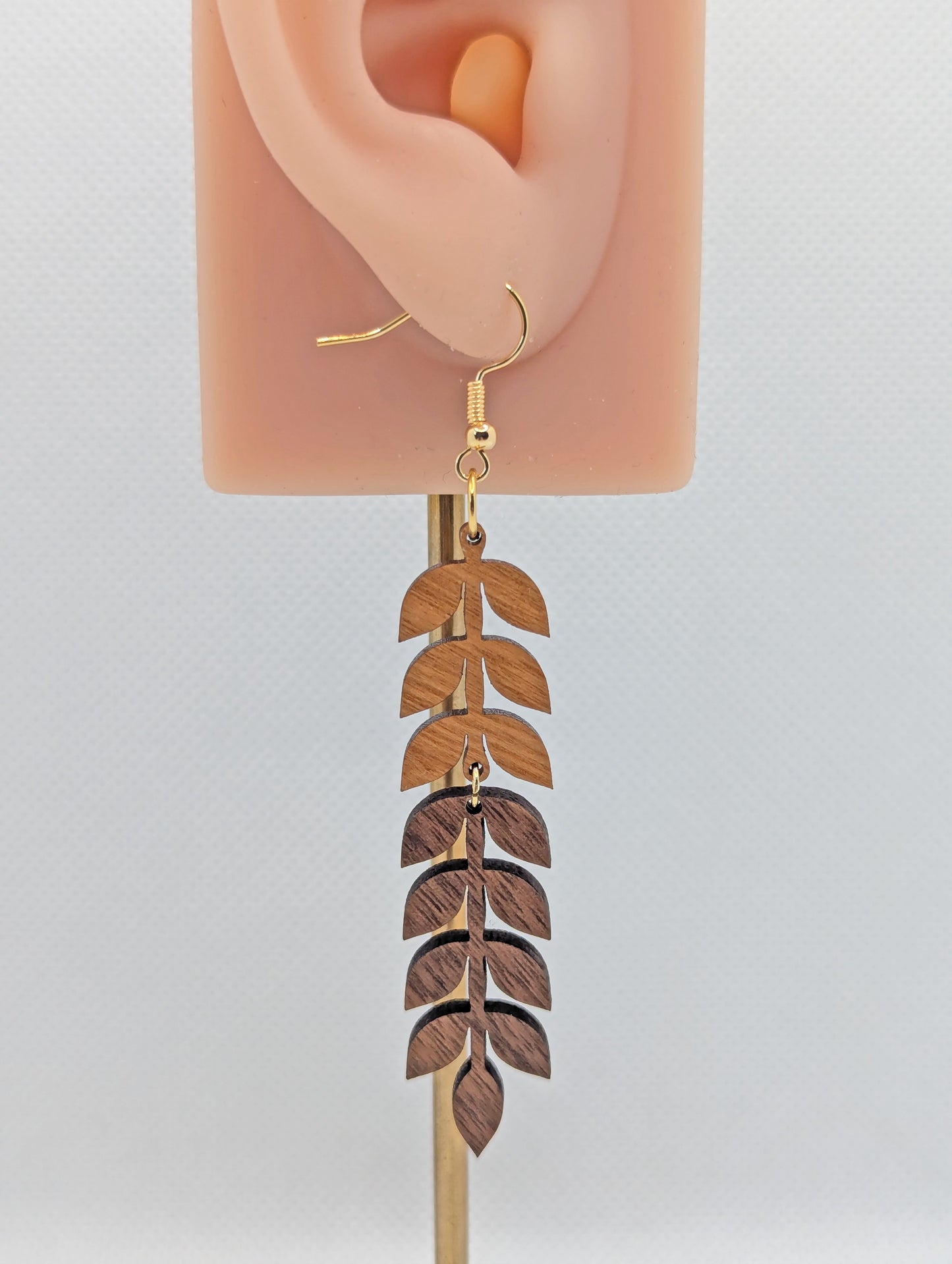 An image of a two part wooden drop earring with Gold ear wire hook fixings. The top part is Cherry Wood and the Bottom part is Walnut Wood. It is on an ear to show the size against a white background.
