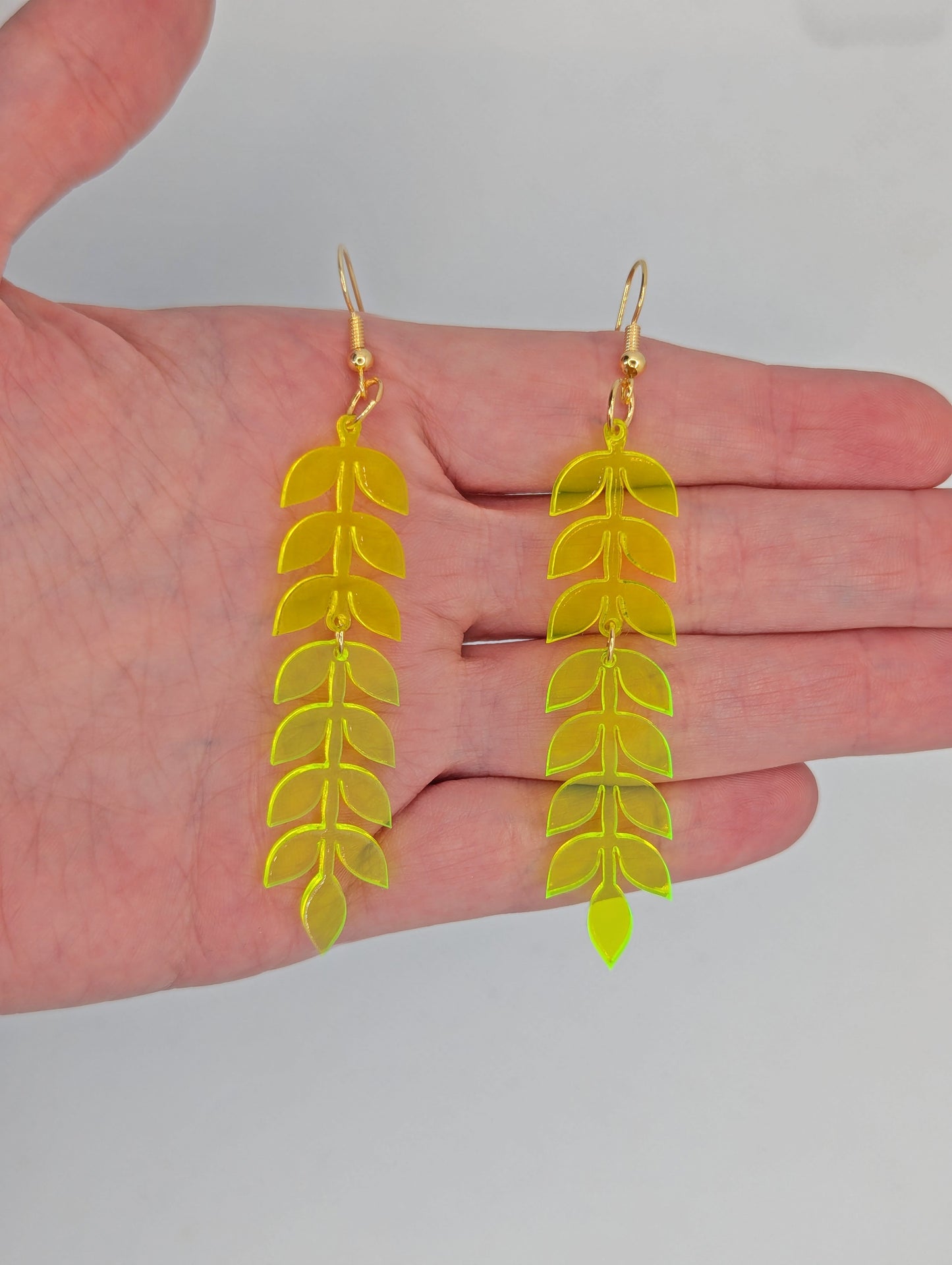 An image of two part acrylic drop earrings with Gold ear wire hook fixings. The top part is Neon Orange and the Bottom part is Neon Yellow. They are against a hand to show the size of four finger widths in length and one wide.