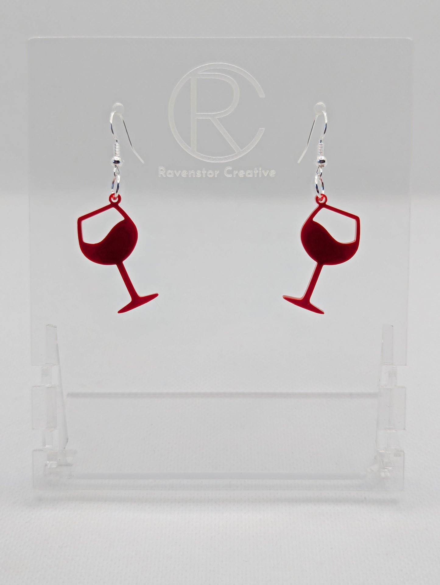 An image of a pair of Wine Glass Earrings with Silver ear wire hook fixings. These are ideal for a Hen Do or Bachelorette Party. The colour is Maroon. They are on clear stands against a white background.