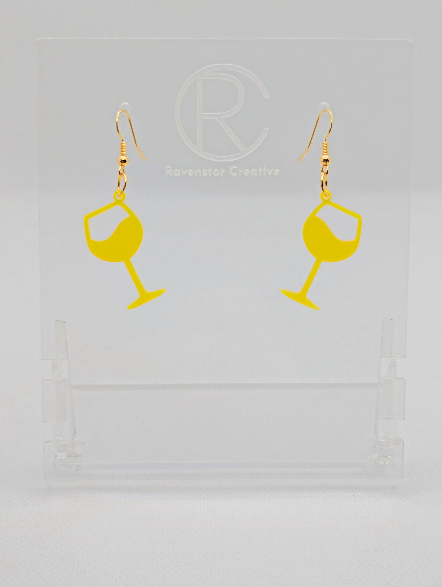 An image of a pair of Wine Glass Earrings with Gold ear wire hook fixings. These are ideal for a Hen Do or Bachelorette Party. The colour is Neon Orange. They are on clear stands against a white background.