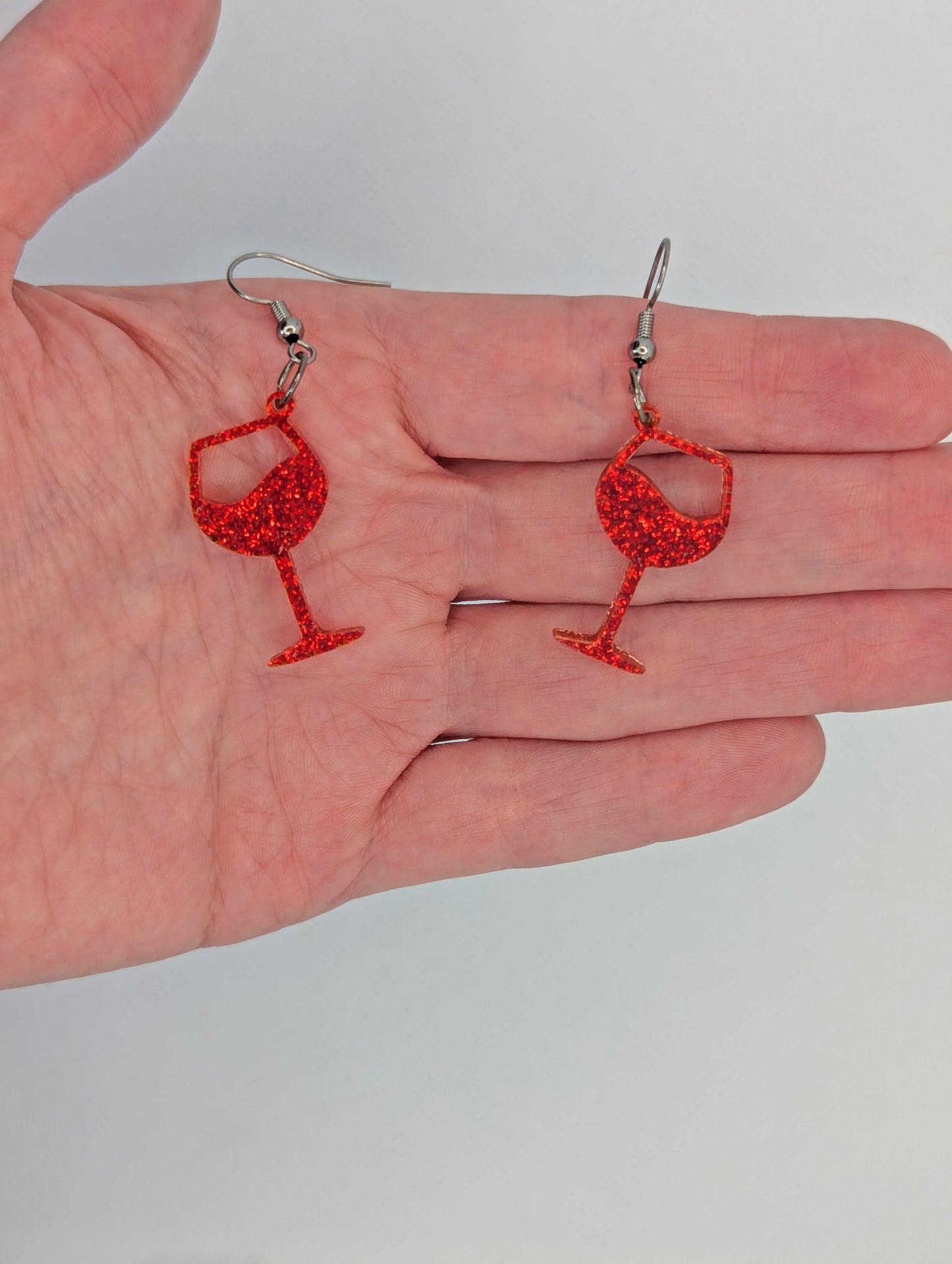 An image of a pair of Champaign Glass Earrings with Black ear wire hook fixings. These are ideal for a Hen Do or Bachelorette Party. They are against a hand to show the size of two finger widths in length and one wide.