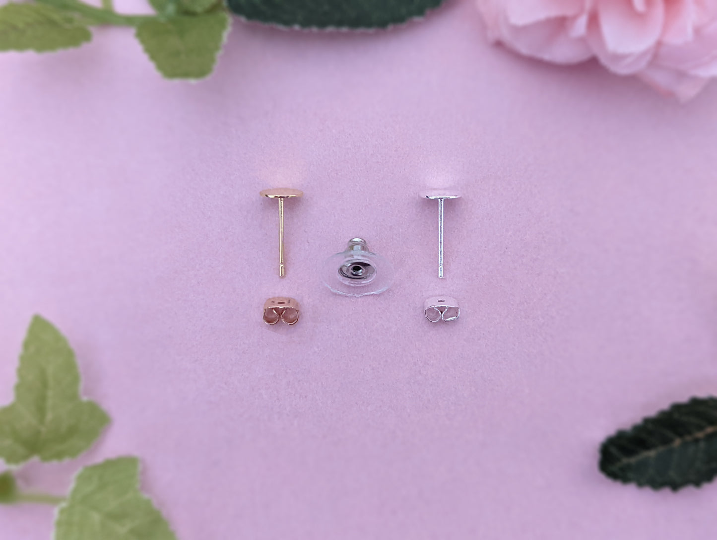 an image of the different fixings these earrings are available with. They are silver and gold with a choice of matching scroll back or a silver large backing. They are displayed on a light pink / purple background with some leaves and a rose head.