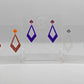 Three pairs of 2 part earrings with stud fixings. The stud is on a small diamond shape with a larger kite shape dangling under. The colours are orange top and Copper glitter bottom, grape top and purple bottom, silver glitter top and clear sparkle