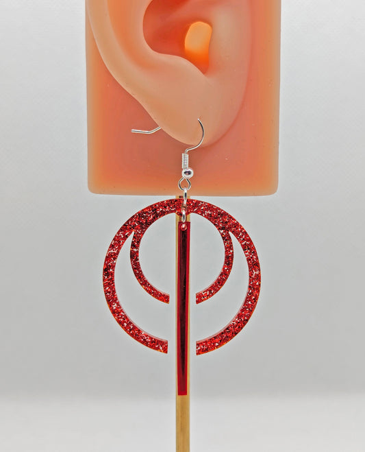 A pair of large double hoop earrings with a gap in the middle and joined at the top, in the gap is a thin dangly pendulum, on an ear showing the size. They are Red Glitter for the hoops and Translucent Red for the dangly pendulum / Pendant.