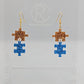 Shows a pair of acrylic earrings with gold ear wire hook fixings. They are Two Jigsaw Game Pieces with one dangling underneath. The colours are copper glitter and royal blue glitter. They are against a white background on a clear stand.