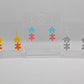 Shows three pairs of acrylic earrings with ear wire hook fixings. They are Two Jigsaw Game Pieces with one dangling underneath. The colours are Yellow and Orange, Spearmint and Sherbet Pink, Silver and Holographic Glitter.