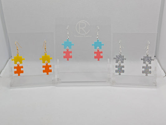 Shows three pairs of acrylic earrings with ear wire hook fixings. They are Two Jigsaw Game Pieces with one dangling underneath. The colours are Yellow and Orange, Spearmint and Sherbet Pink, Silver and Holographic Glitter.