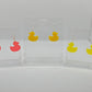 Shows three pairs of earrings that have ear wire hook fixings. They are rubber Duck / ducky shaped with ear wire hook fixings. The colours are Neon pink, yellow and neon Yellow. They are against a white background on see through stands.