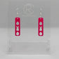 A pair of acrylic earrings that have Silver ear wire hook fixings. They are slim long bar pendant earrings with three Easter egg and rabbit / bunny shapes cut out. They are Hot Pink in colour and are against a white background on see through stand.