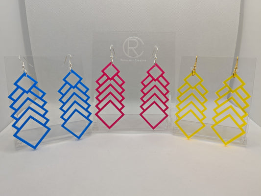 Three pairs of large acrylic earrings. They are long Geometric diamond shaped. They have ear wire hook fixings and the colours are Blue, hot pink and neon yellow. They are on clear stands against a white background.