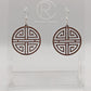 Shows a pair of earrings that have silver ear wire hook fixings. They are Geometric Korean Inspired Circle earrings with an intricate pattern like a maze. They are walnut wood and are against a white background on see through stand.