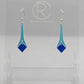 Shows a pair of earrings with silver ear wire hook fixings. They are slim teardrop geometric shapes in two parts with a diamond shape dangling under. The colours are spearmint top and blue diamond. They are on a clear stand against a white backing