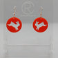 A pair of acrylic earrings that have Rose Gold ear wire hook fixings. They are Circles with an Easter bunny / Rabbit hopping down cut out each one. It is Red colour. They are against a white background on see through stands.