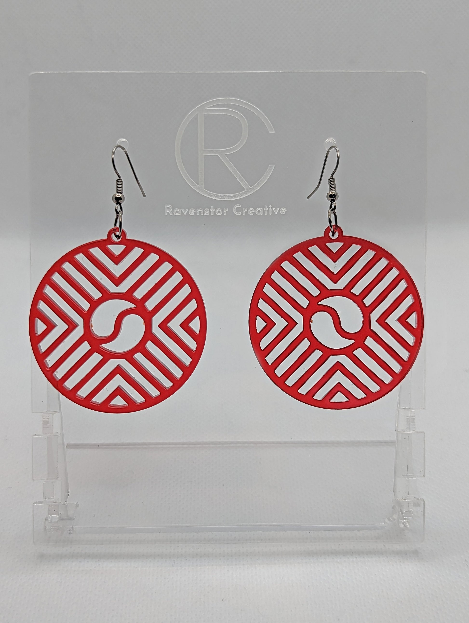 Shows a pair of Circle earrings that have black ear wire fixings. They are Geometric Chevron designs with a yin and yang in the centre. They are made from Red Acrylic. They are against a white background on see through stands.